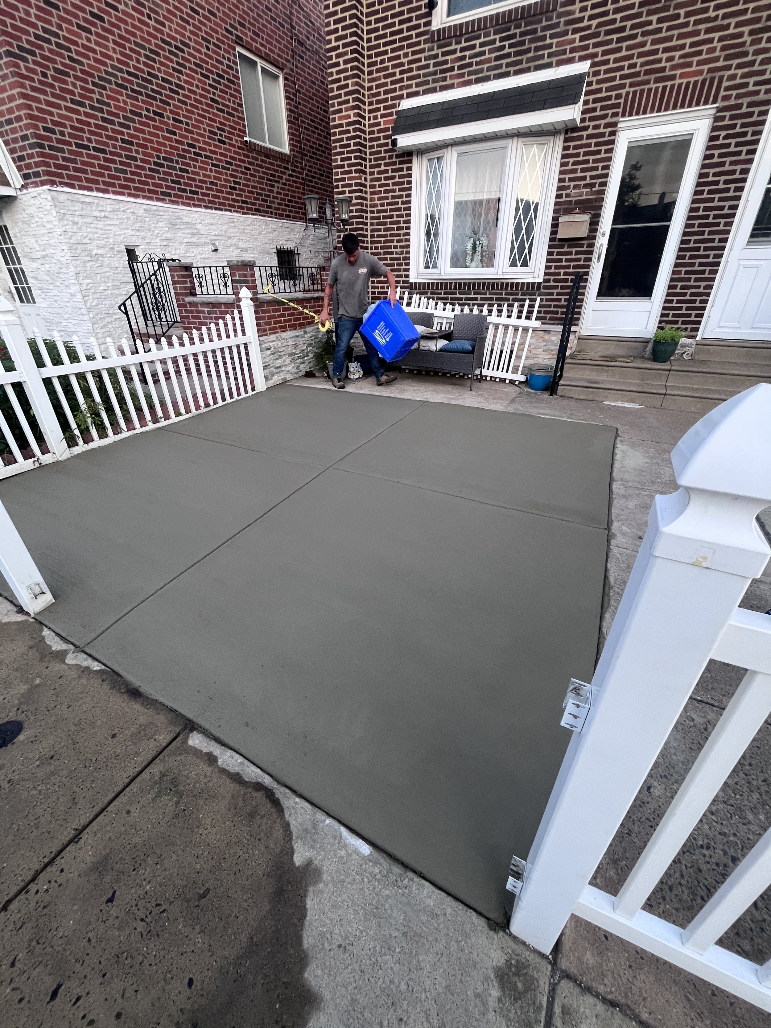 A person pouring concrete into a sidewalk area in front of a brick house.