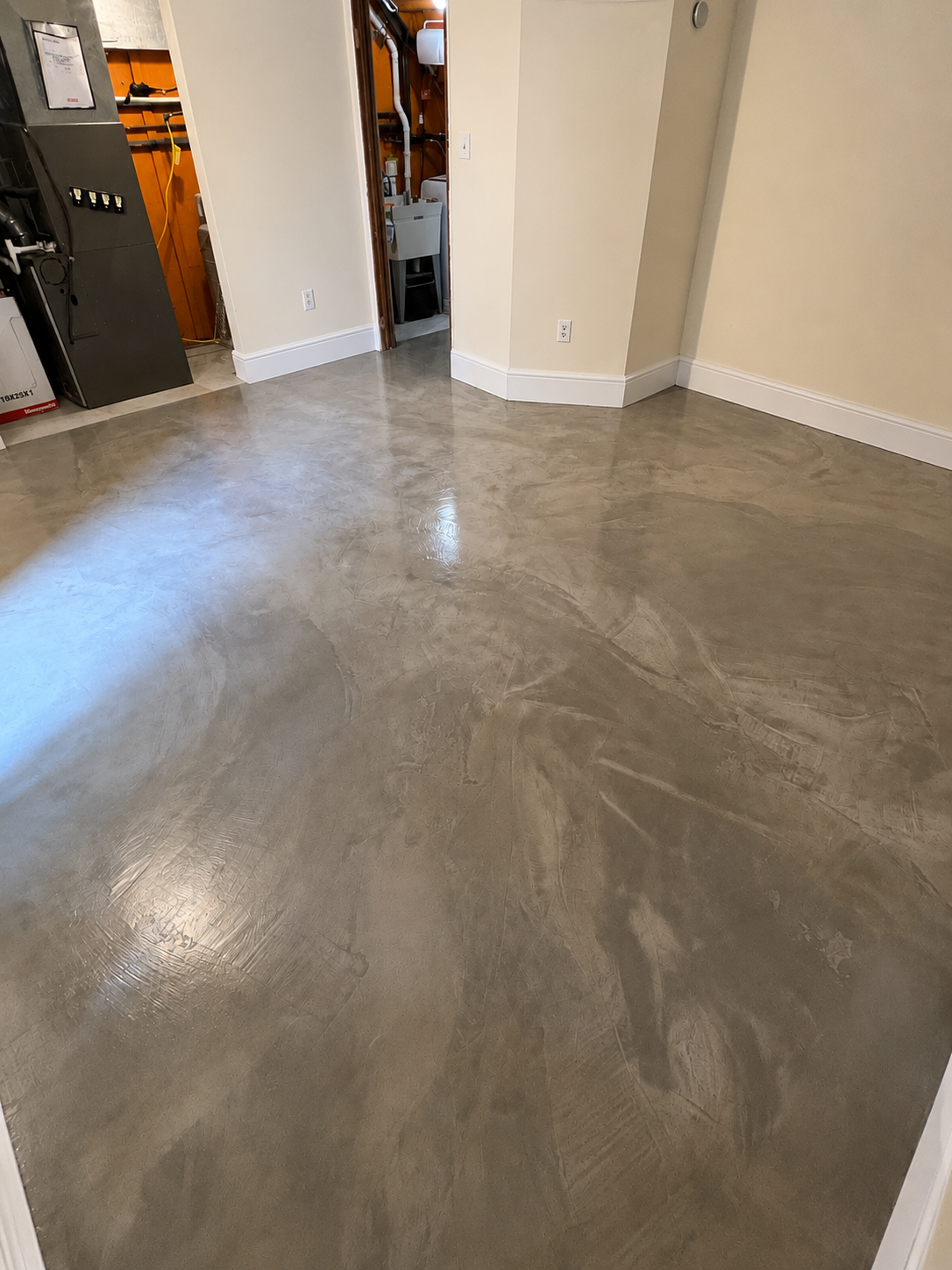 Finished concrete floor with a glossy, smooth surface in a room with white walls, a doorway, and electrical outlets.