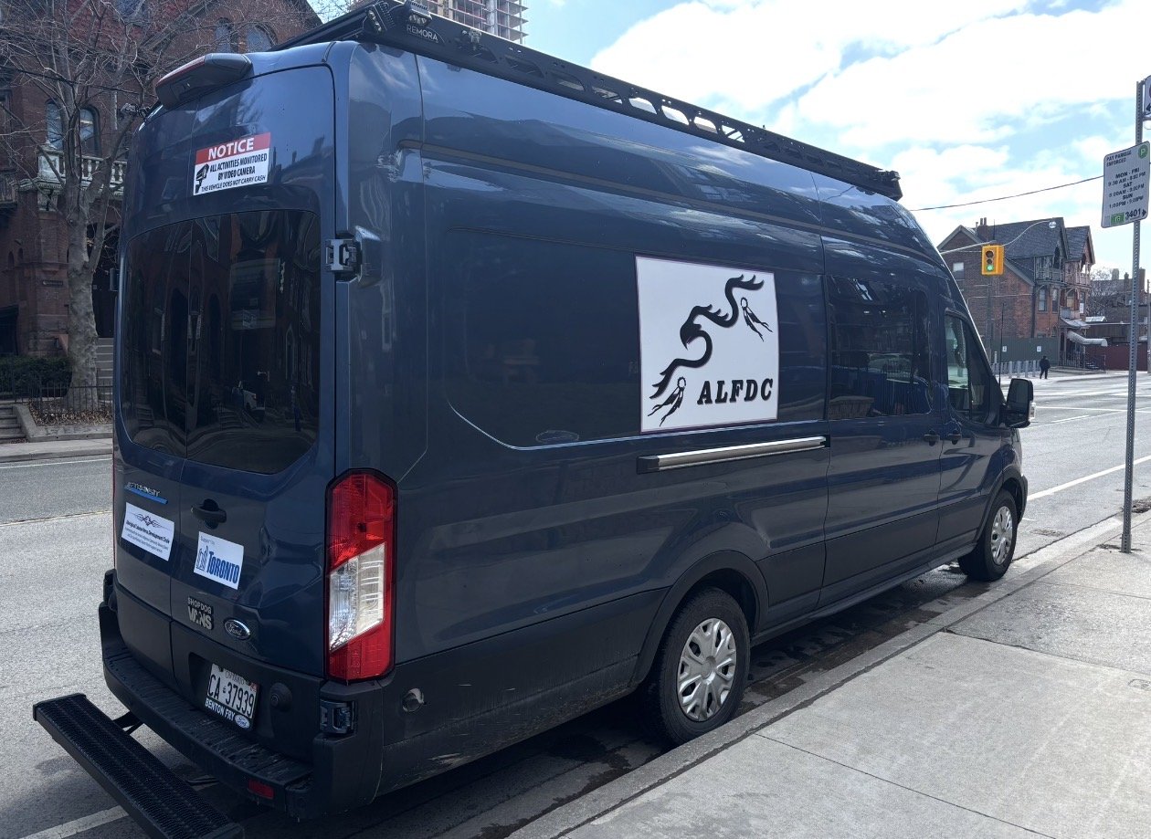 A dark blue van parked on a city street with a logo of a dragon and the letters ALFDC on the side.