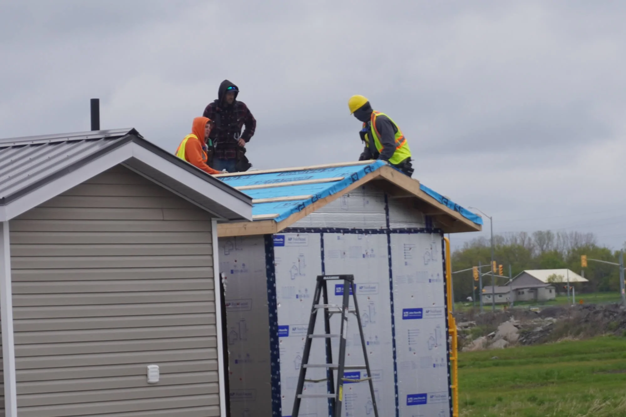 Community members participating in a hands-on ALFDC construction workshop, utilizing safety gear and tools while roofing.