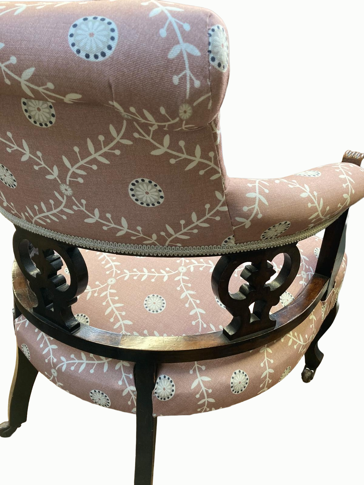 An antique wooden rocking chair with pink fabric upholstery decorated with white floral and circular patterns.