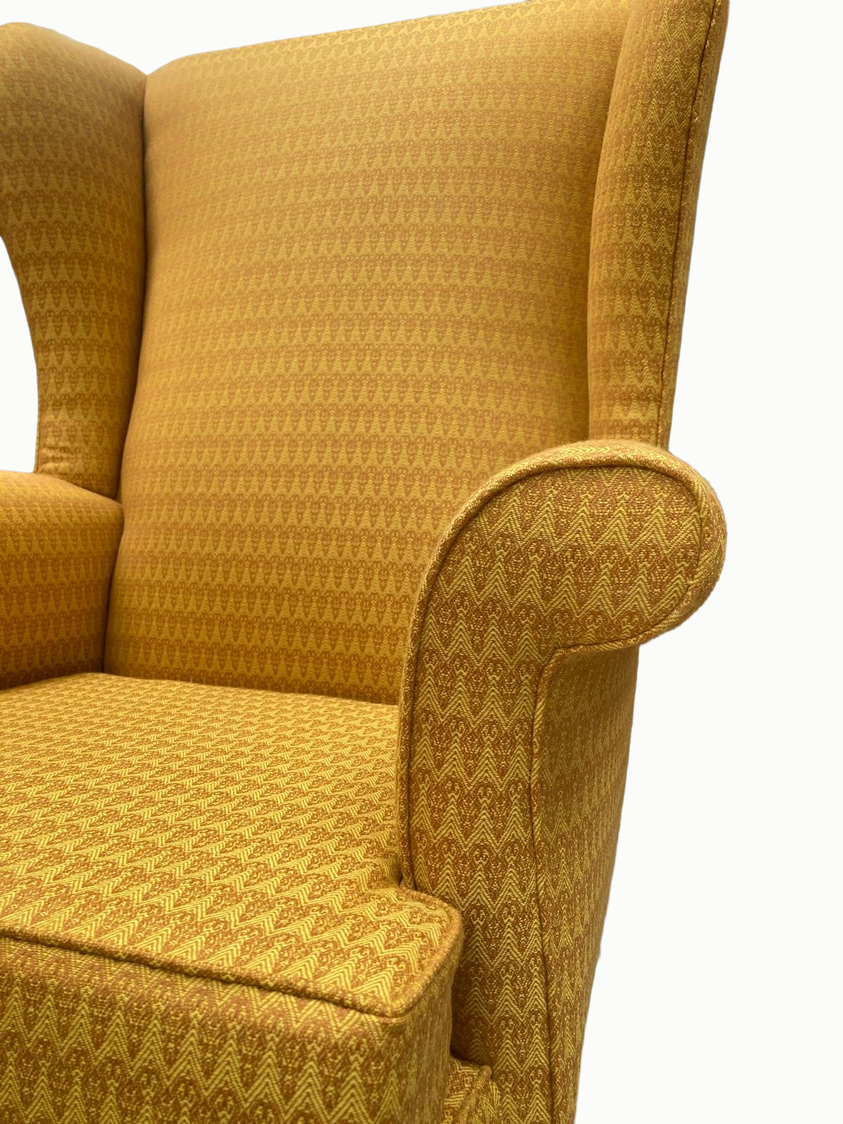 Close-up of a vintage mustard-yellow upholstered armchair with patterned fabric, high back, rounded armrest, and a matching ottoman.