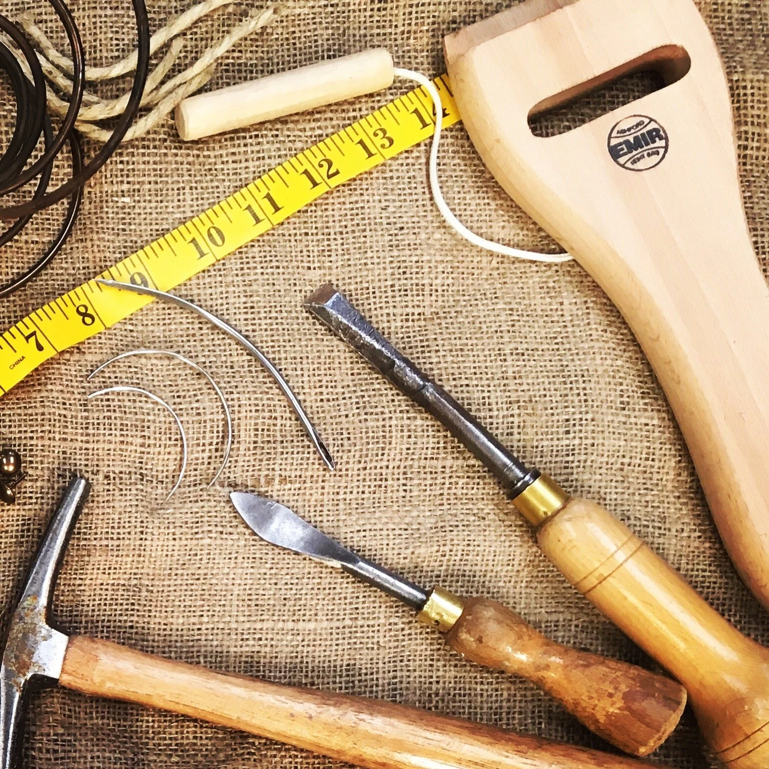 Various woodworking tools on a burlap surface, including a tape measure, a hammer, a chisel, and a hand saw.