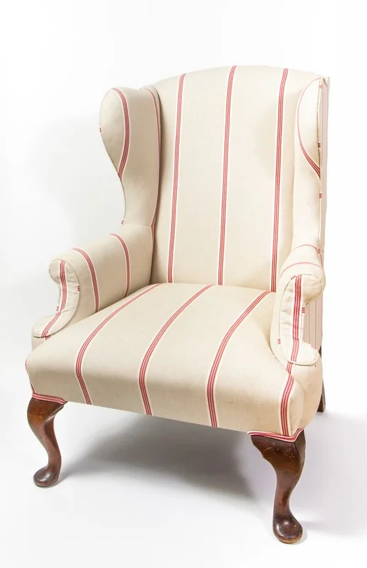 A vintage wingback armchair with white fabric and red vertical stripes, wooden cabriole legs, and padded armrests.