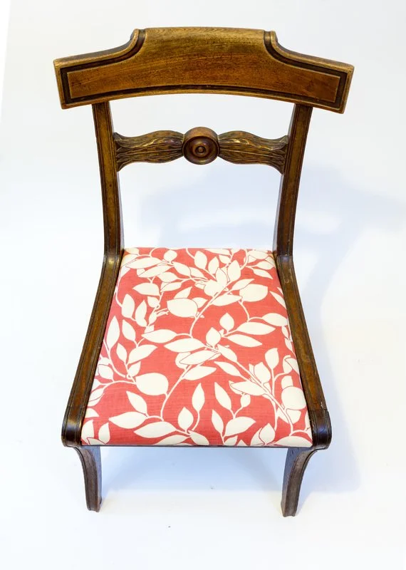 A wooden chair with a carved backrest and a cushioned seat with a red and white leafy pattern.