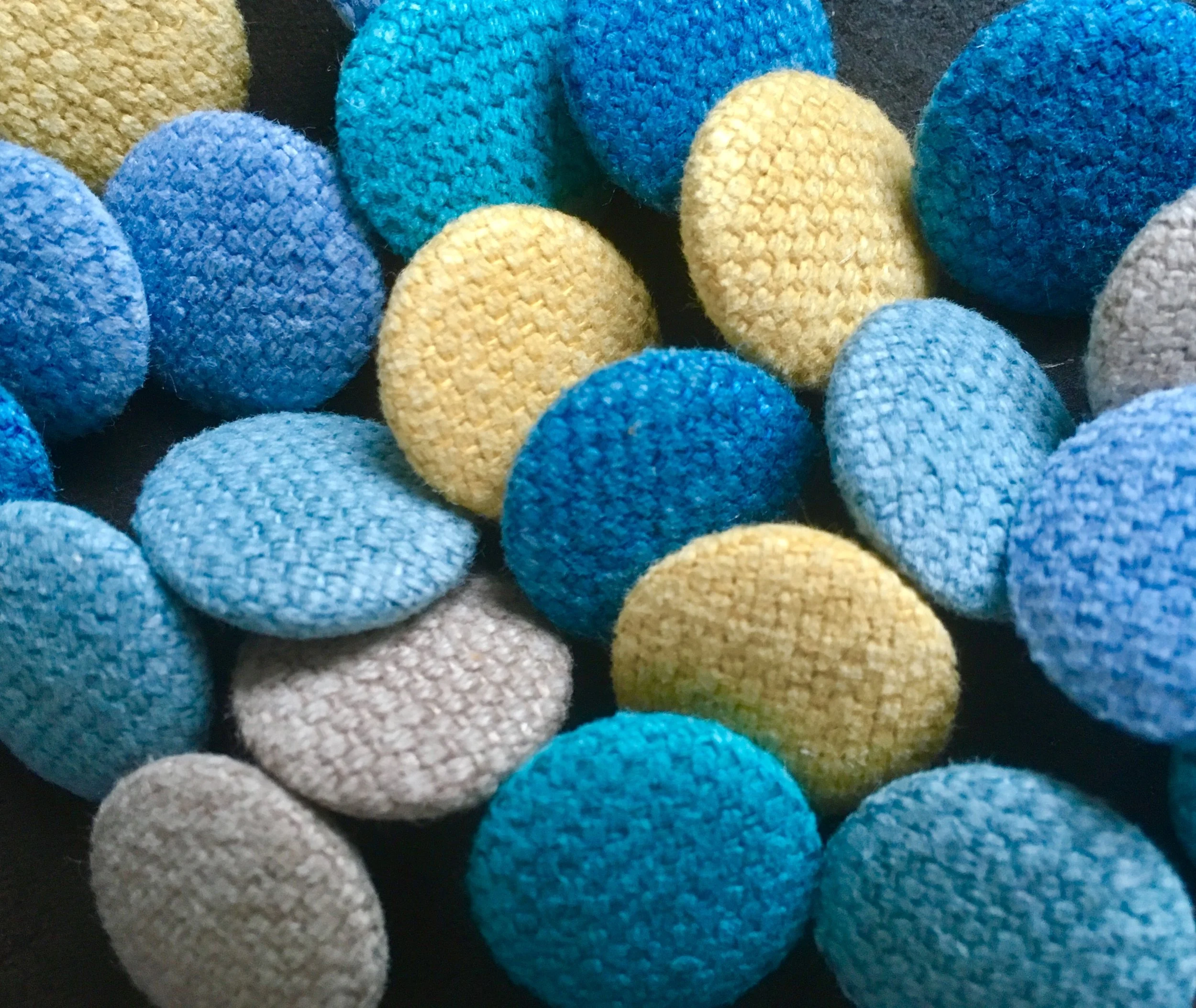 A close-up view of multicolored textured buttons, primarily in shades of blue, yellow, and gray, on a dark background.