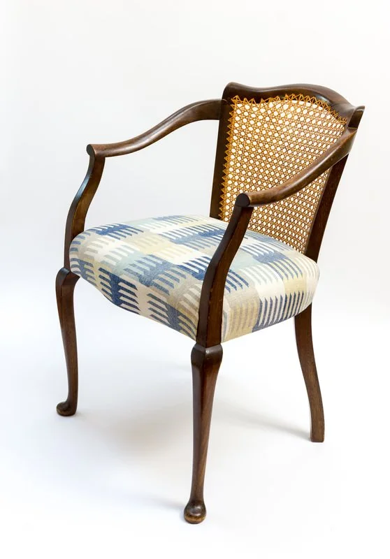 A wooden armchair with a cane backrest and a patterned upholstered seat, set against a white background.