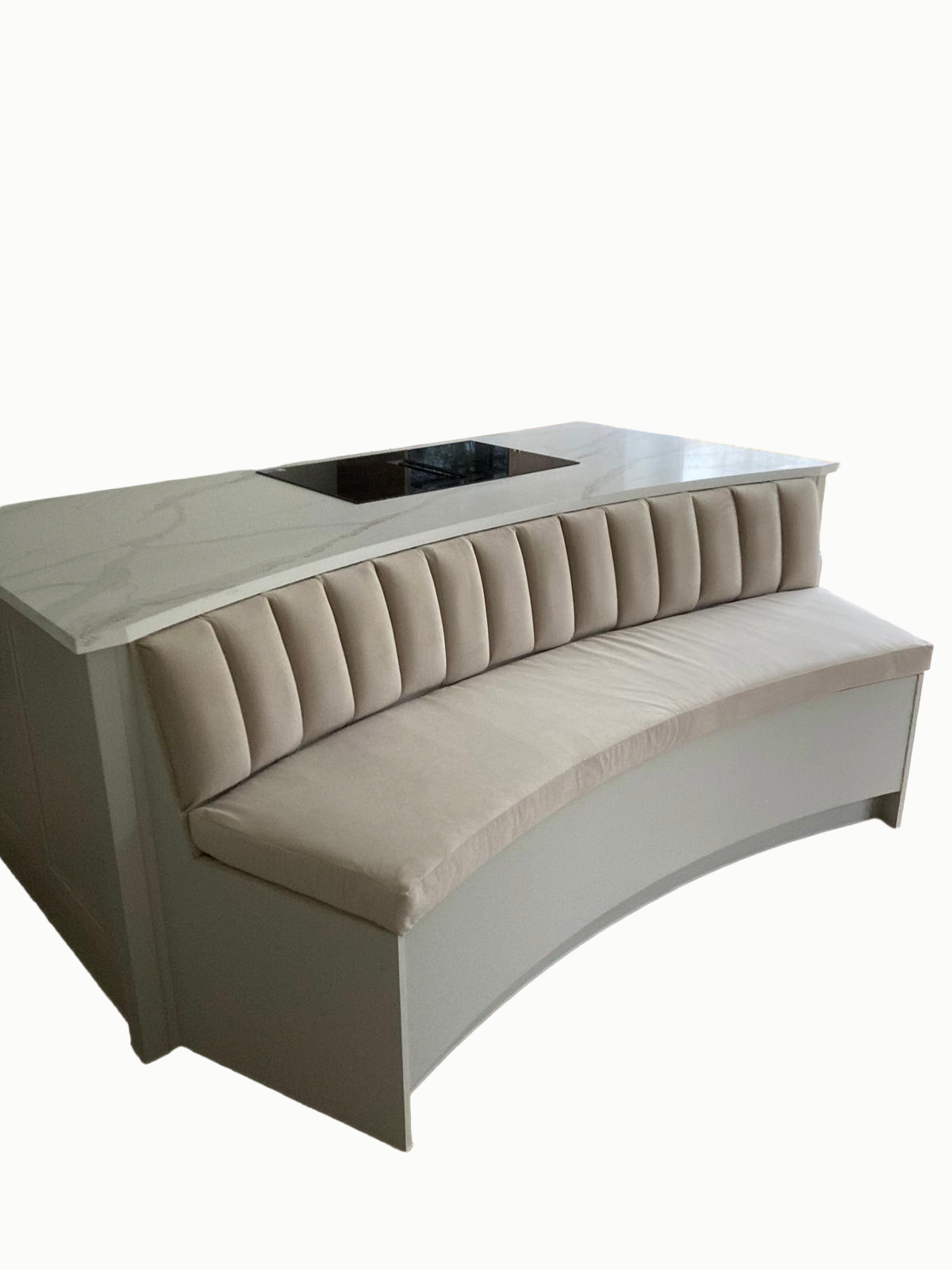 A curved beige banquette with vertical tufted upholstery and a white marble countertop with gray veining, featuring an electric cooktop built into the surface.