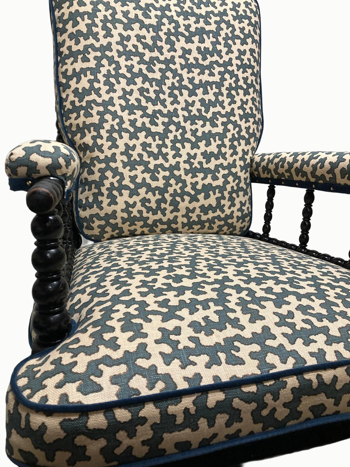 Close-up of an upholstered armchair with a patterned fabric in blue and beige, featuring wooden armrests and turned wooden legs.