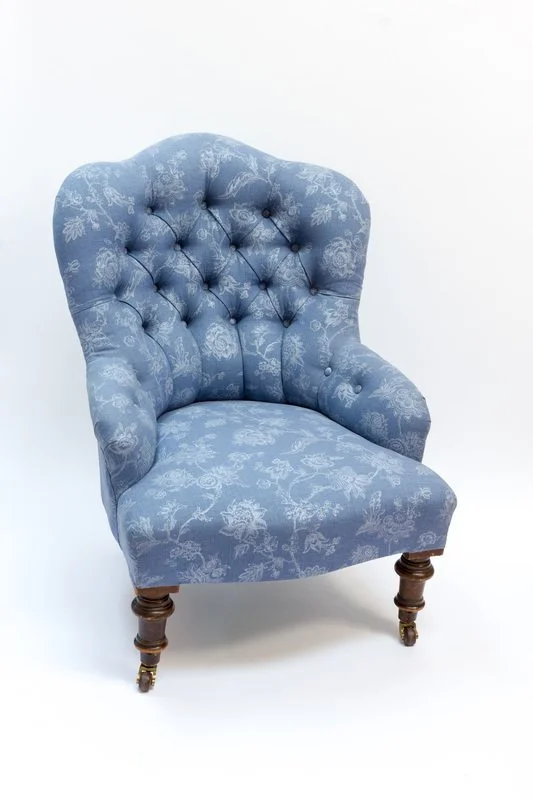 A vintage blue upholstered armchair with a floral pattern and wooden legs with casters.