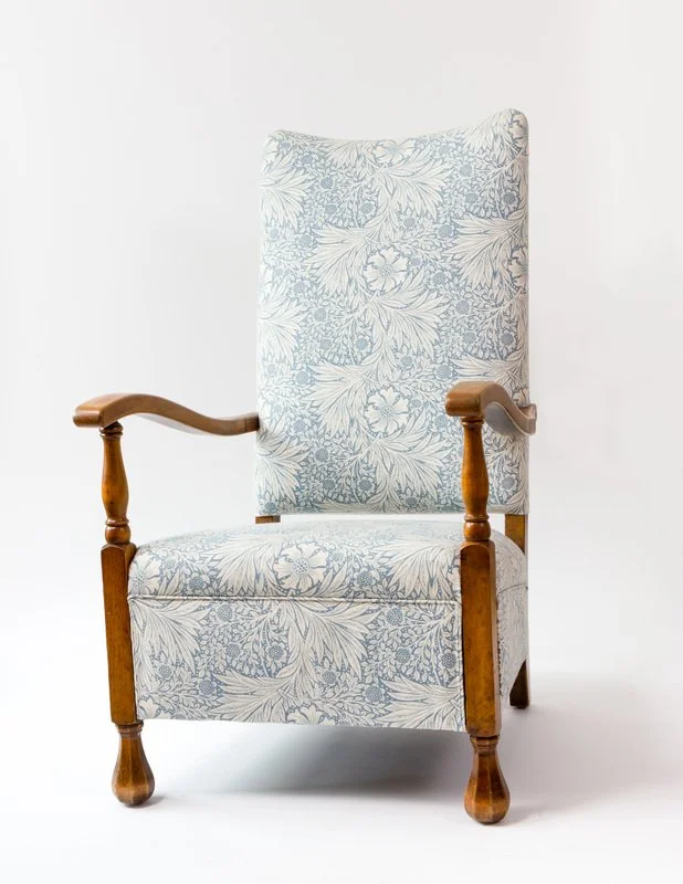 A vintage armchair with a high back, wooden arms, and carved wooden legs, upholstered in a light blue and white floral fabric.