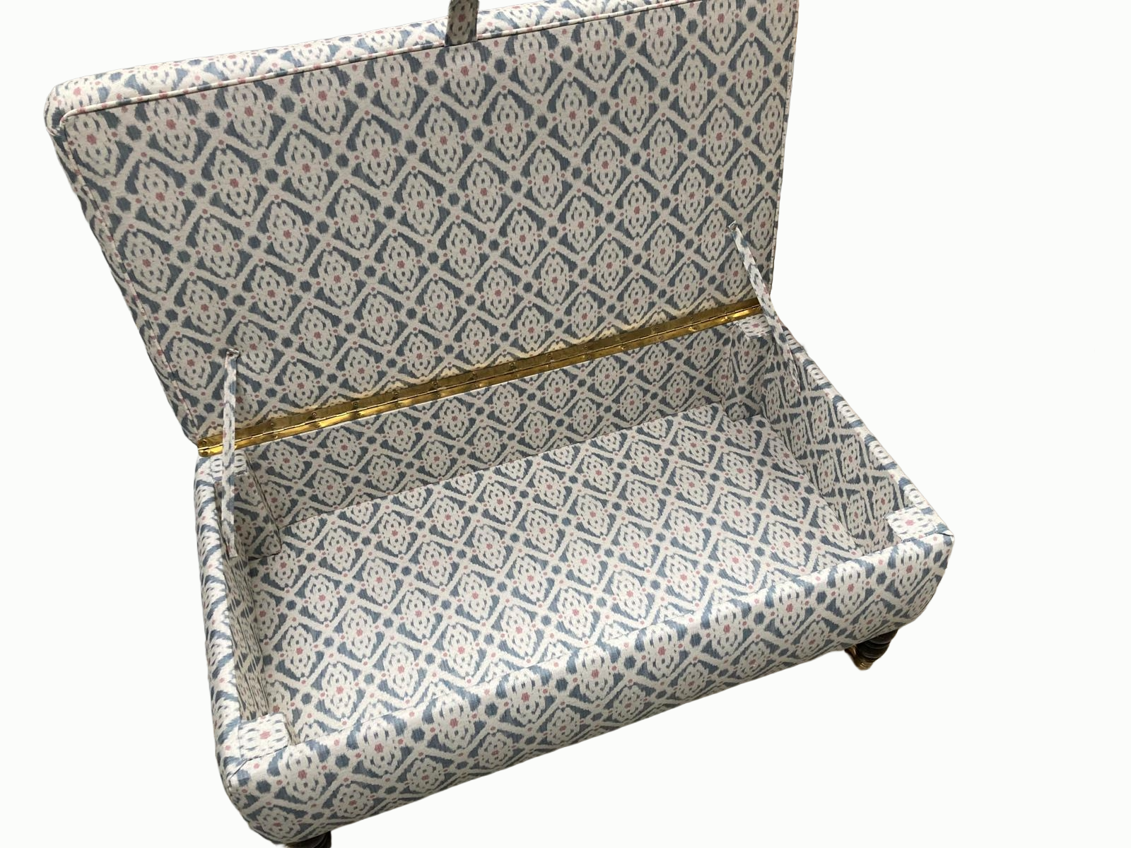 An open antique-style fabric-covered storage chest with a geometric pattern in blue, cream, and pink. The interior and exterior are lined with matching patterned fabric, and the lid is held open with fabric straps.