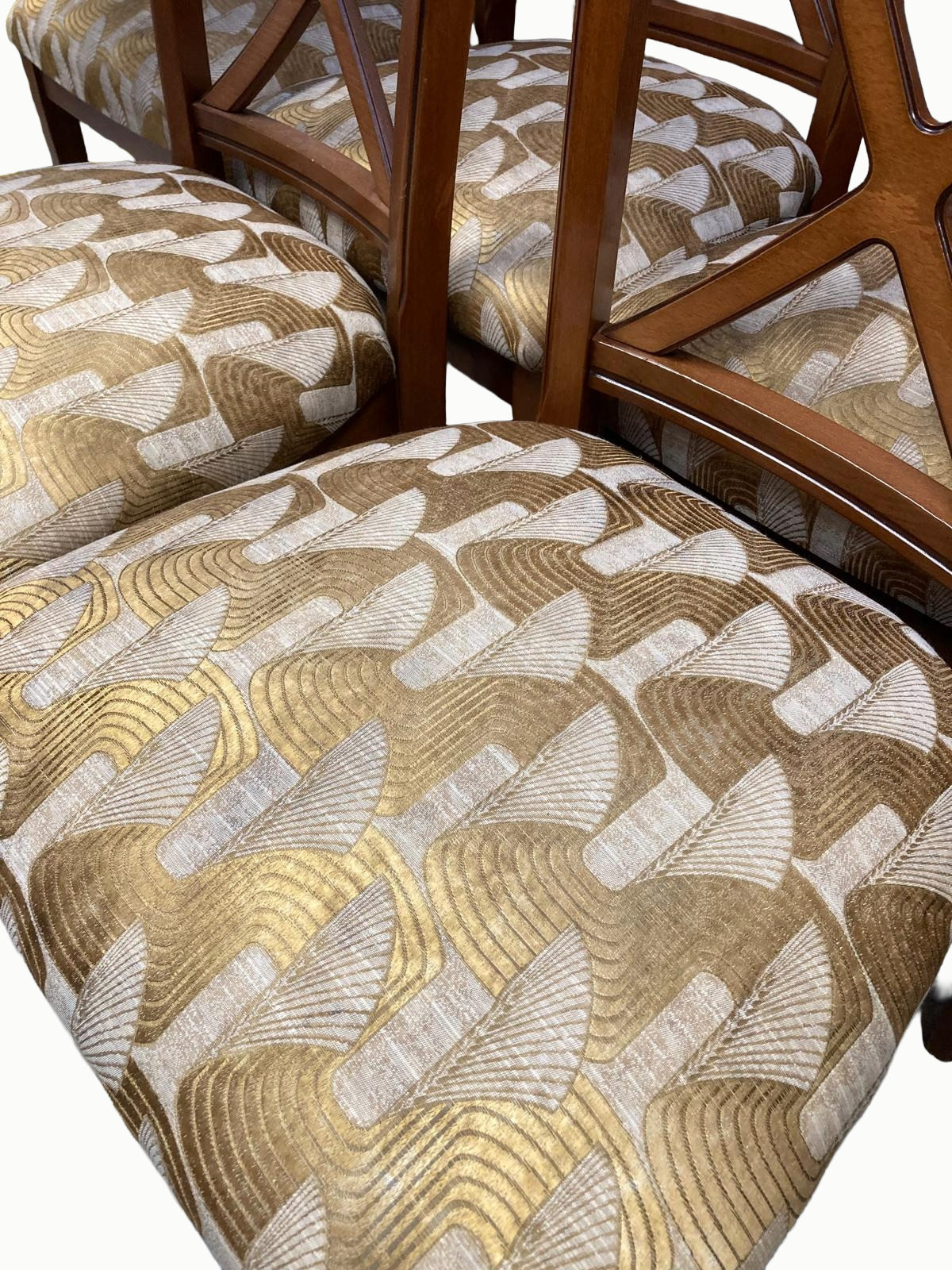 Several wooden chairs with patterned fabric seats and backs, featuring a geometric fan and wave design in gold, brown, beige, and gray colors.