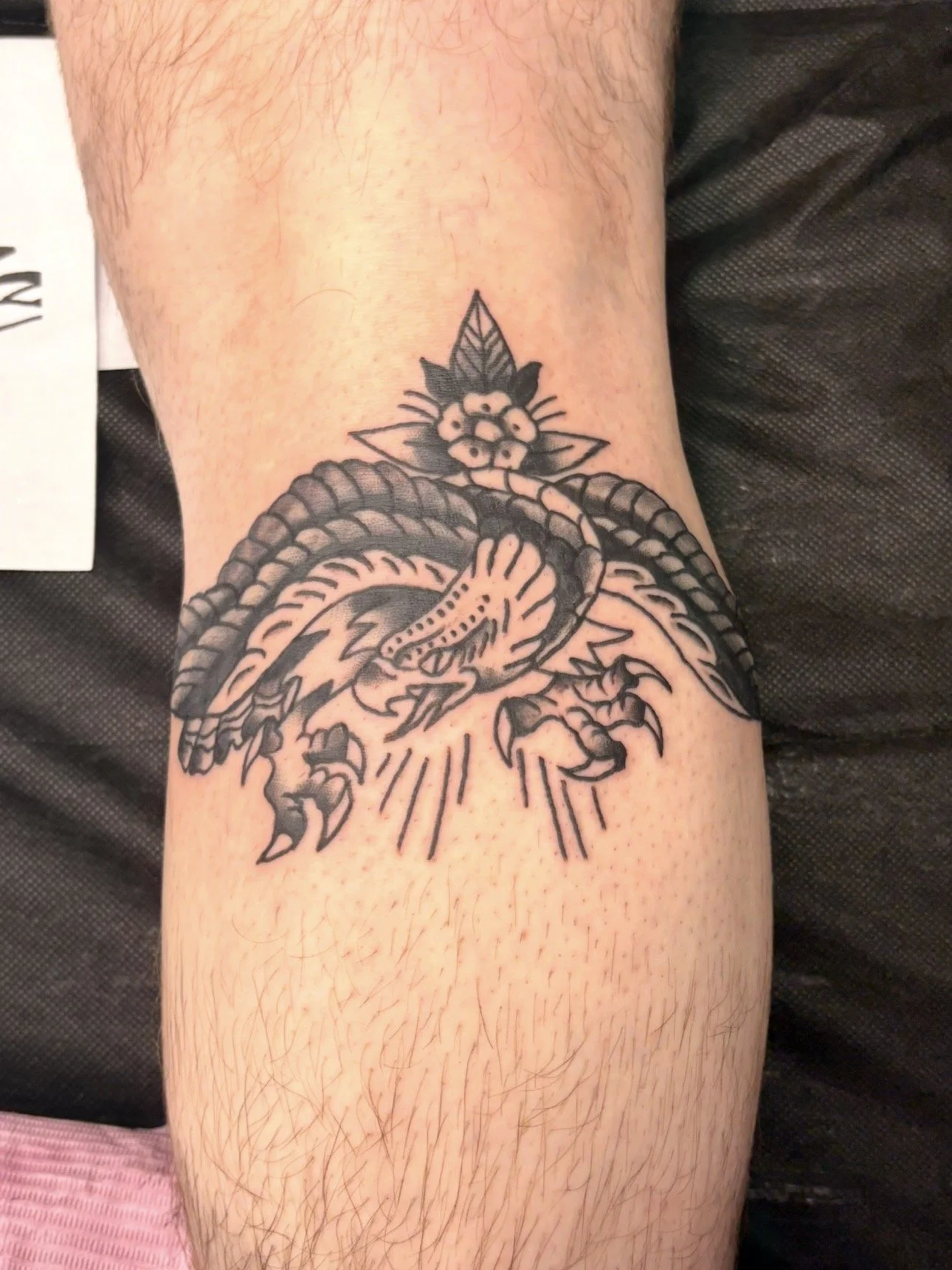 Tattoo of a dragon on a person's leg, with stylized details and smoke or fire effects.