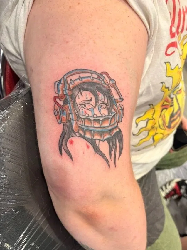 Tattoo of a woman with tears on their face inside a helmet on a person's upper arm.