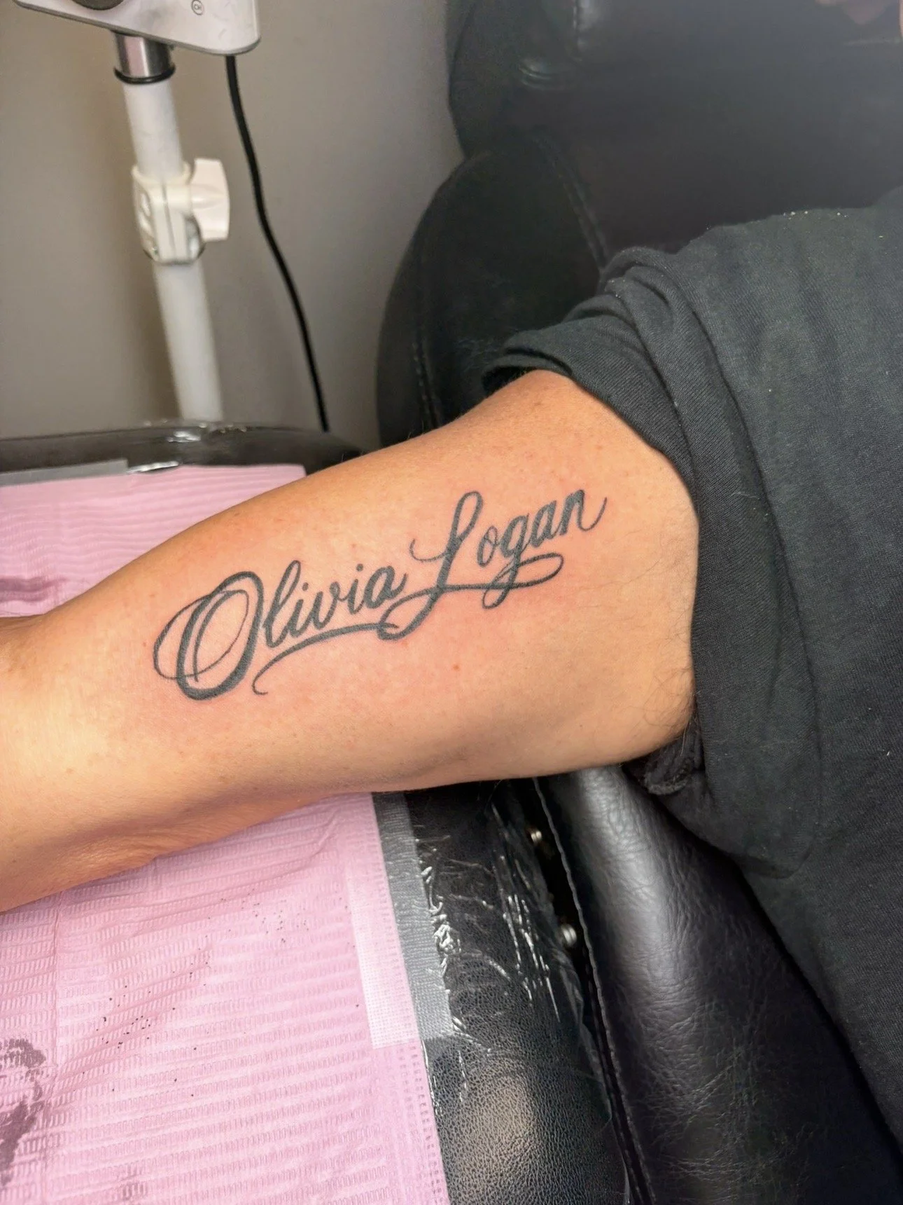 Tattoo of the name 'Olivia Logan' in cursive on a person's forearm.