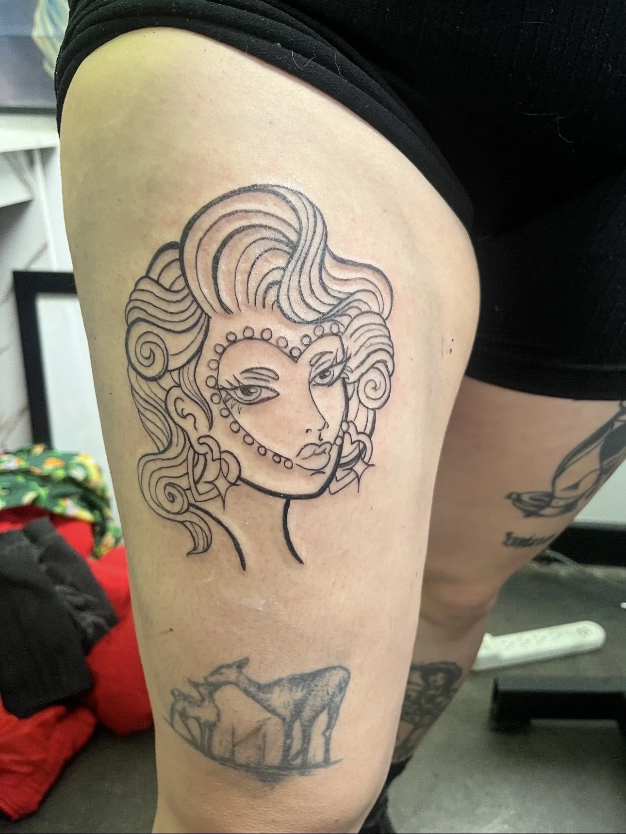 Line drawing tattoo of a woman with flowing hair and decorative facial markings on a person's upper arm.