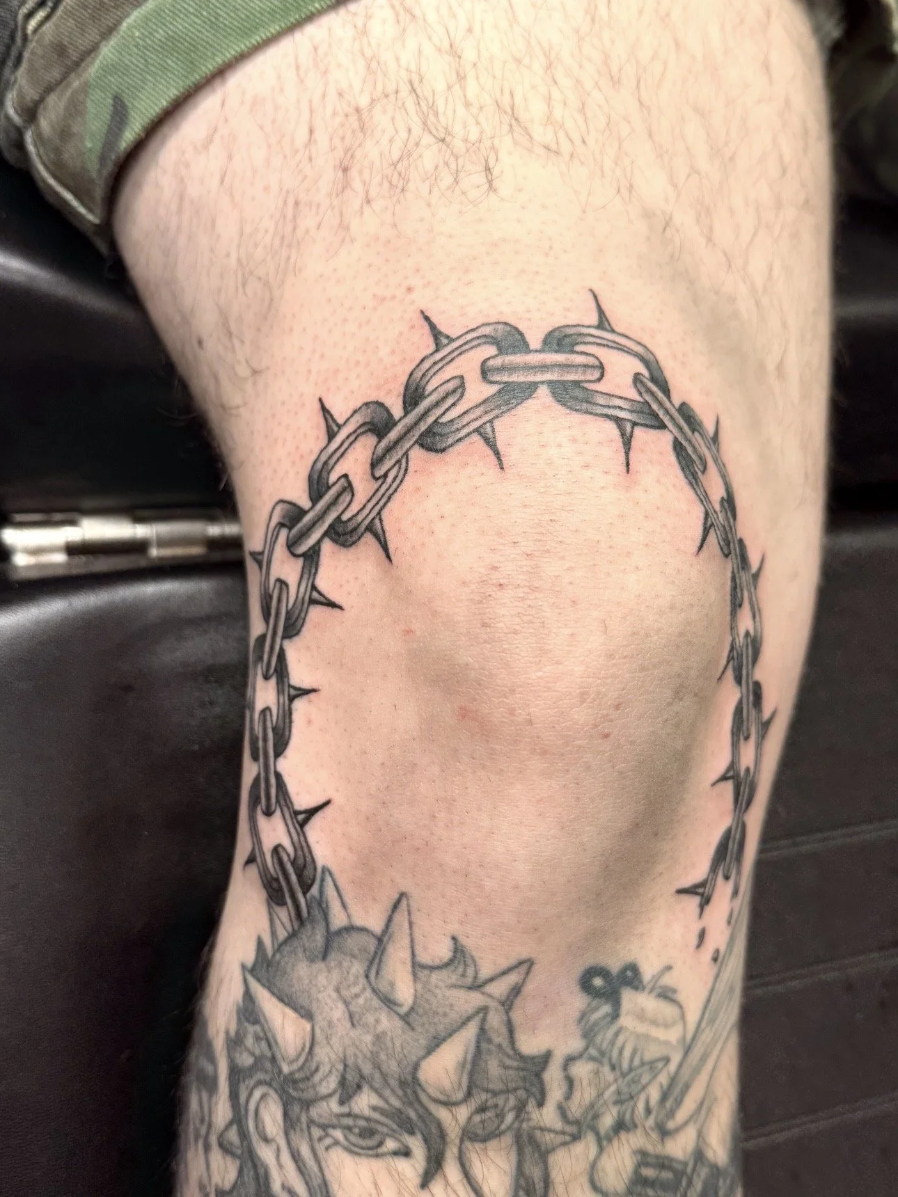 Tattoo of a barbed chain wrapping around the upper arm with some spiked and floral designs below.