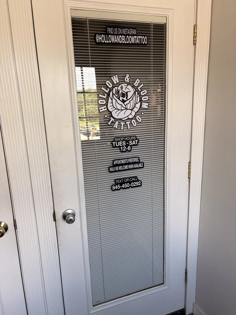 Sign on a door advertising Hollow & Bloom Tattoo, with shop hours, appointment info, and social media handle, featuring a logo of a skull and snake.