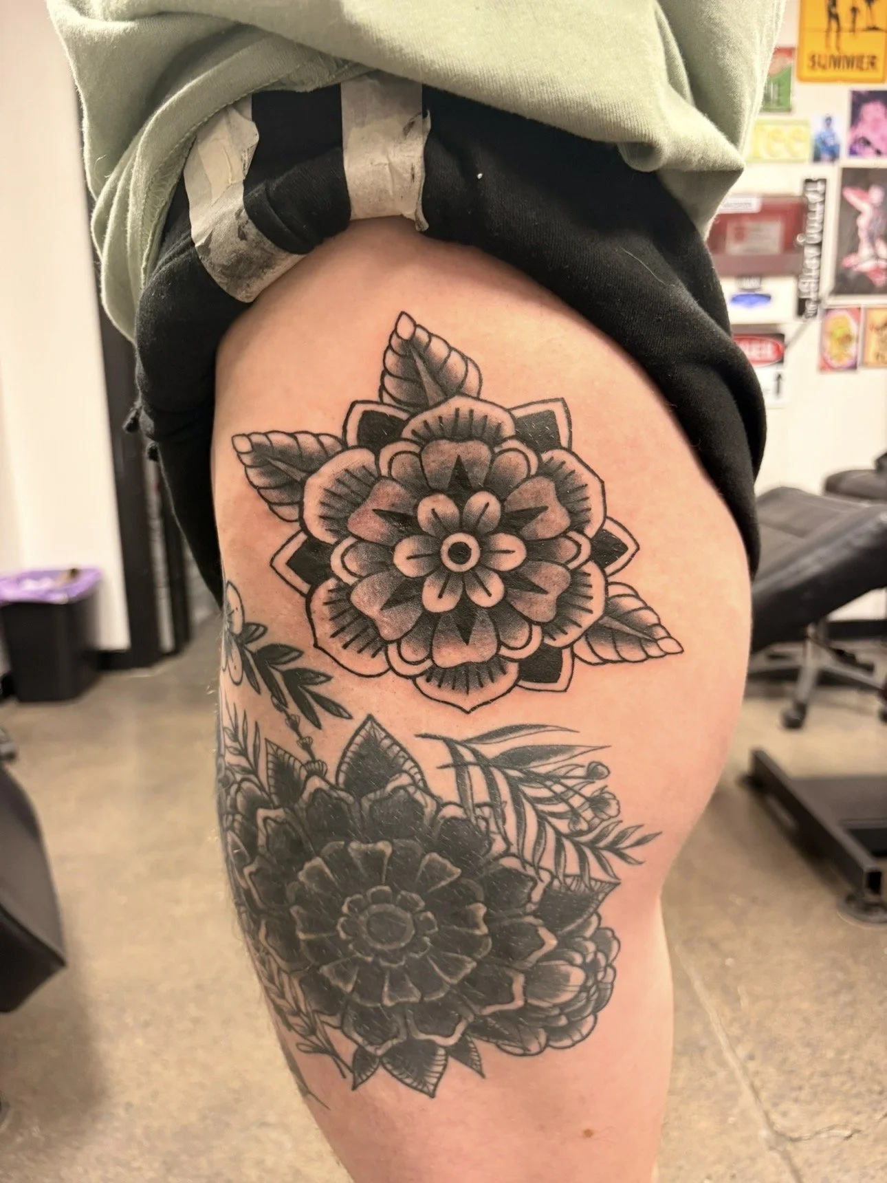 Black and gray floral tattoo sleeve on a person's upper thigh and part of the hip, featuring large flowers, leaves, and intricate line work.