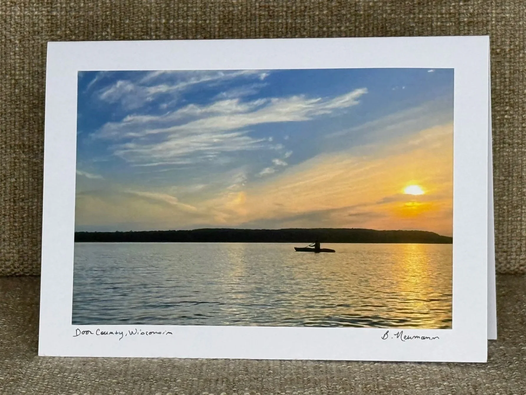 A photo of a boat on a lake during sunset with colorful clouds and a tree-lined horizon.