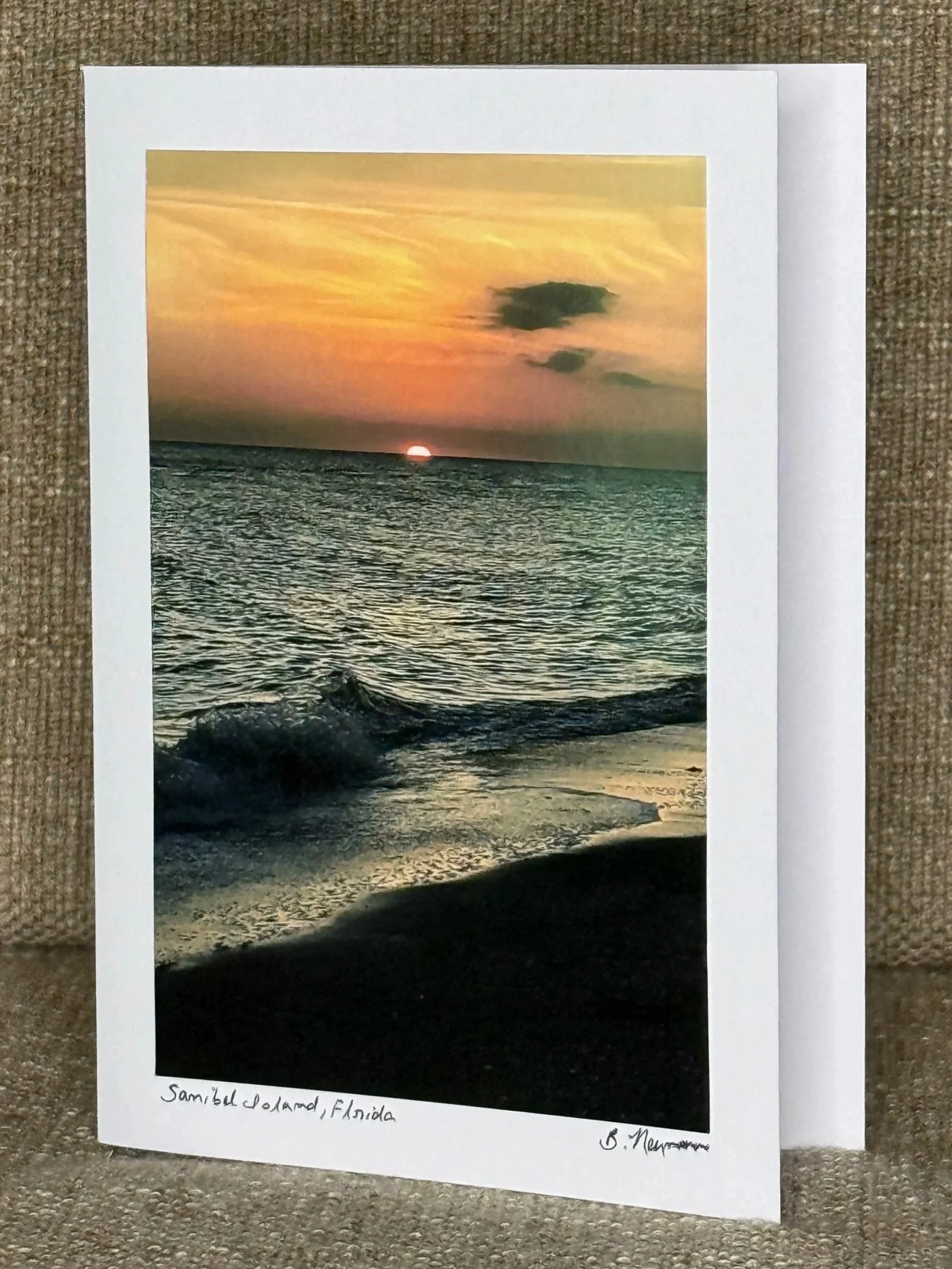 Photograph of a sunset over the ocean with clouds and a horizon line, printed on a piece of paper with some handwritten text at the bottom reading 'Sambel Island, Florida'.