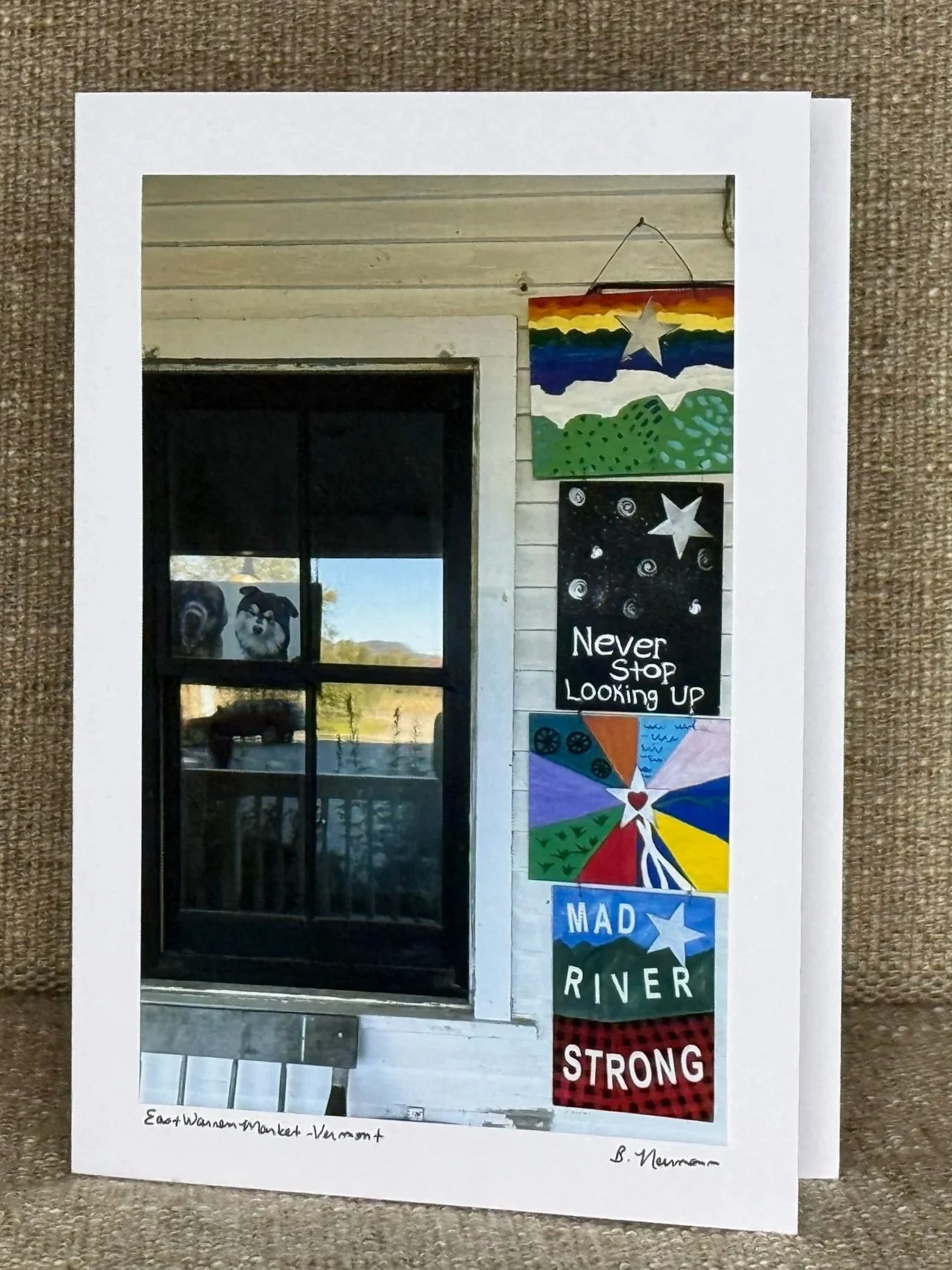 A sheet of paper with a picture of a building window and colorful painted posters with motivational messages hanging on the wall outside. The posters have inspirational phrases like "Never Stop Looking Up," "Mad River," and "Strong," with star images