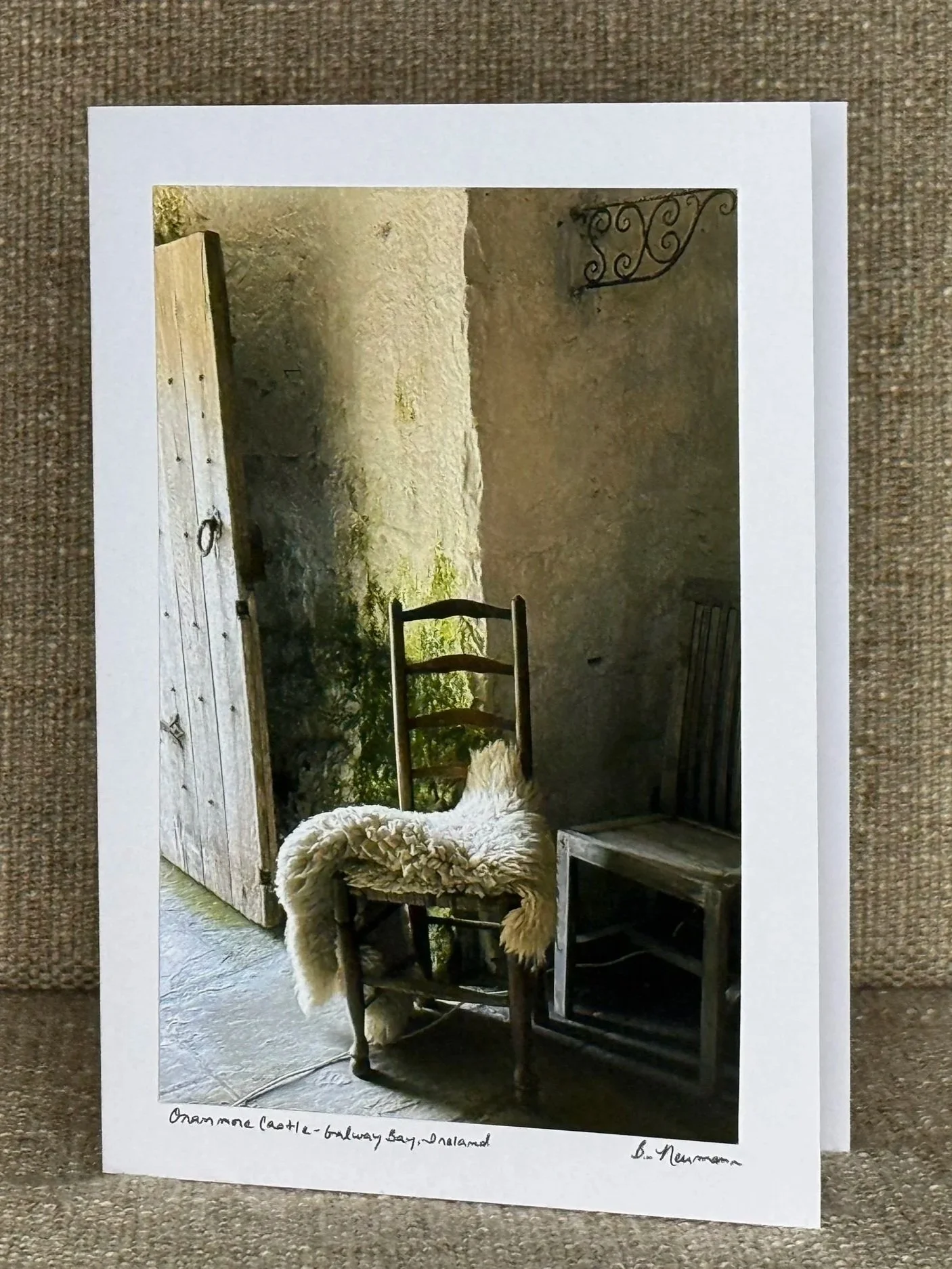 A photograph of an outdoor scene showing a wooden door, a sheep rug draped over a wooden chair, and other rustic furniture pieces, with a stone wall in the background.