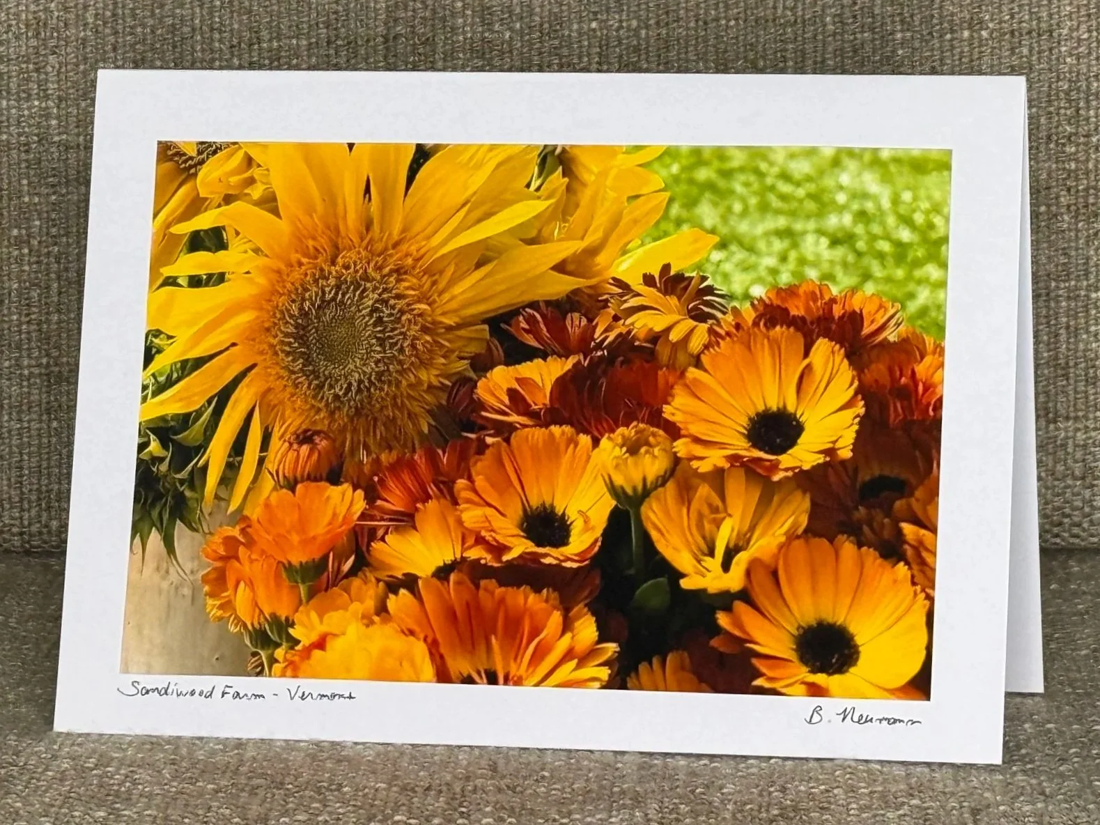 Photograph of a vibrant bouquet of yellow and orange flowers, including sunflowers and daisies, on a white border with handwritten notes at the bottom.
