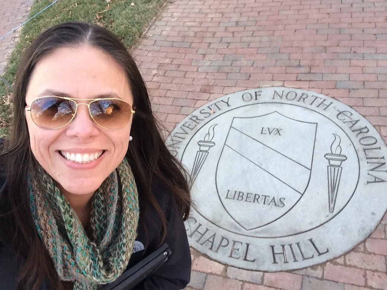 Smiling woman with sunglasses and scarf taking a selfie on Chapel Hill belonging to the University of North Carolina.