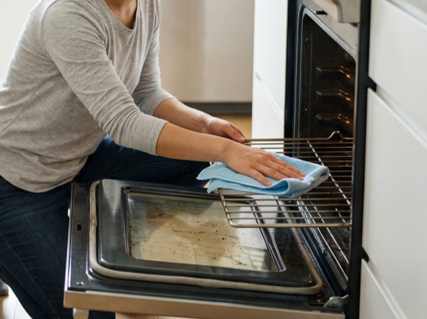 Person wearing a gray long-sleeve shirt cleaning an oven with a cloth.