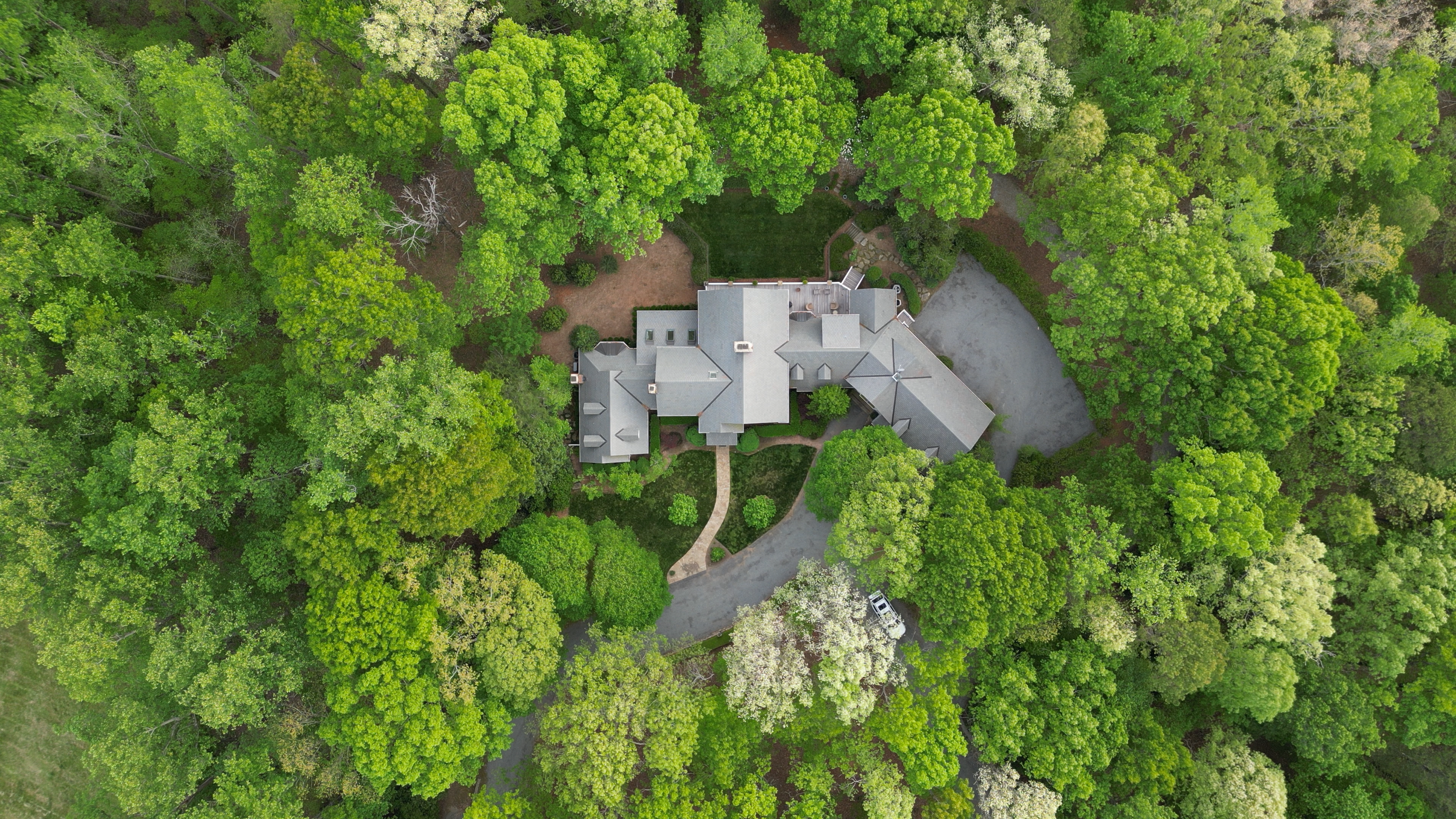 Aerial view of a house surrounded by dense green trees and a driveway.