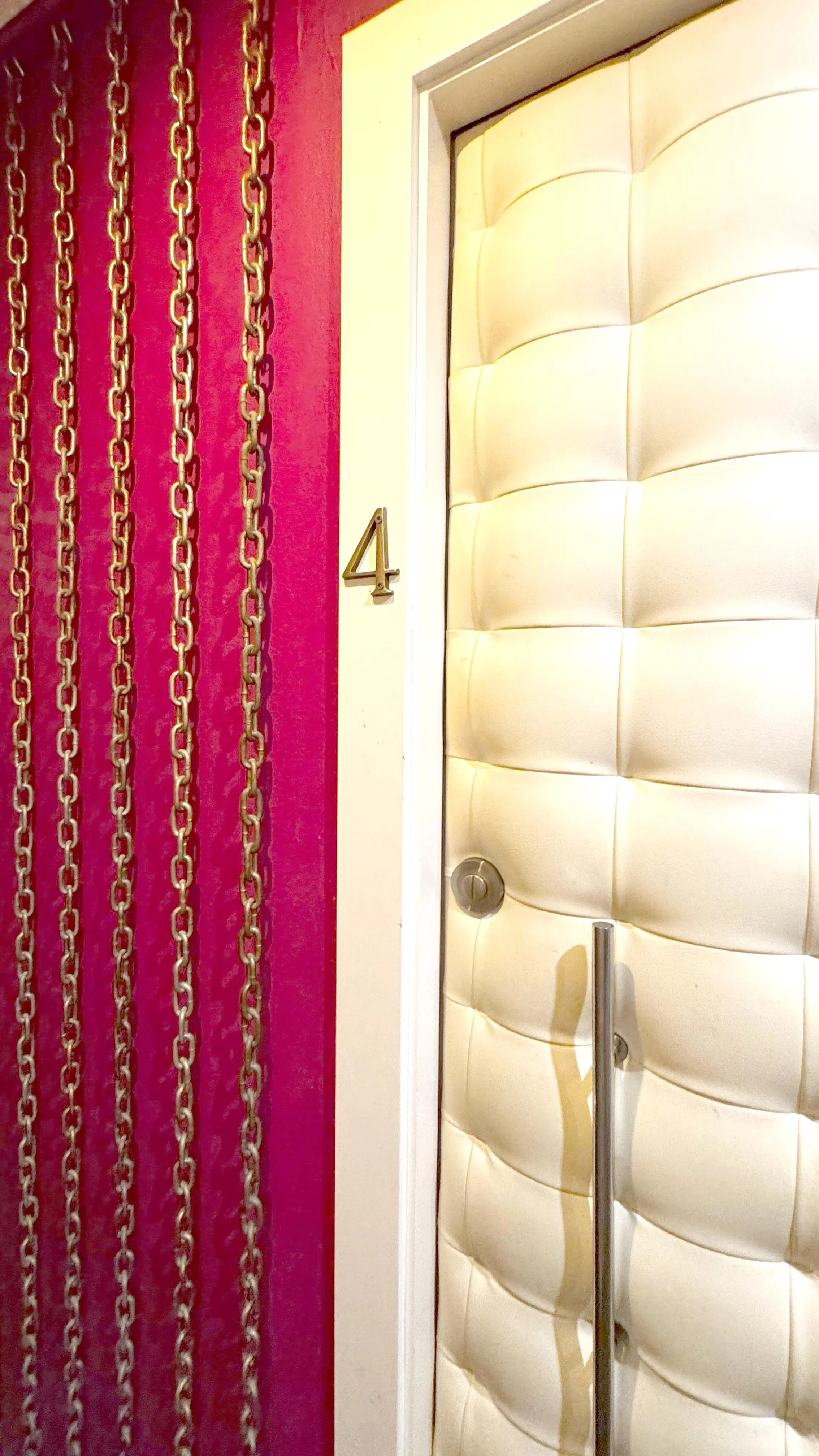 Número 4 en la pared junto a puertas de ascensor con tapizado beige y cortinas rojas con cadenas doradas.