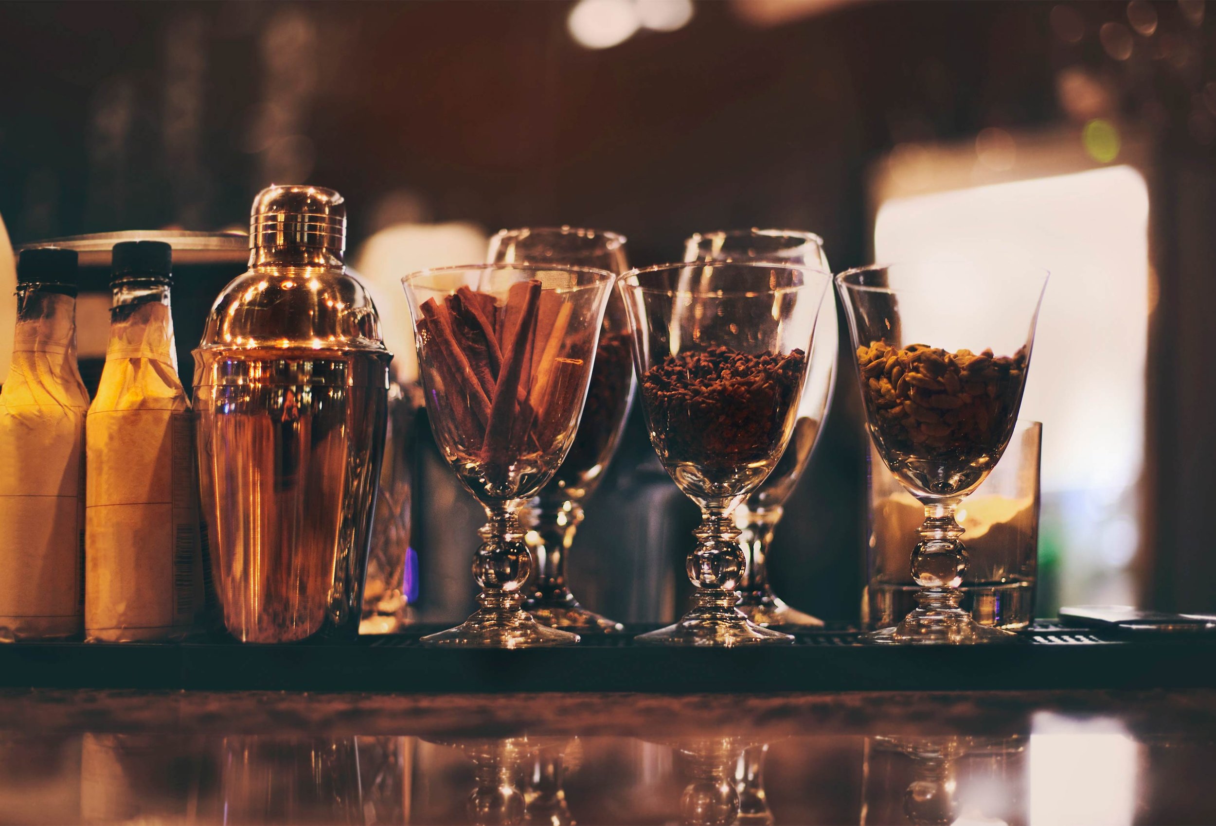 Vasos de cristal con especias y plantas aromáticas en un bar o café, con iluminación cálida y ambiente acogedor.