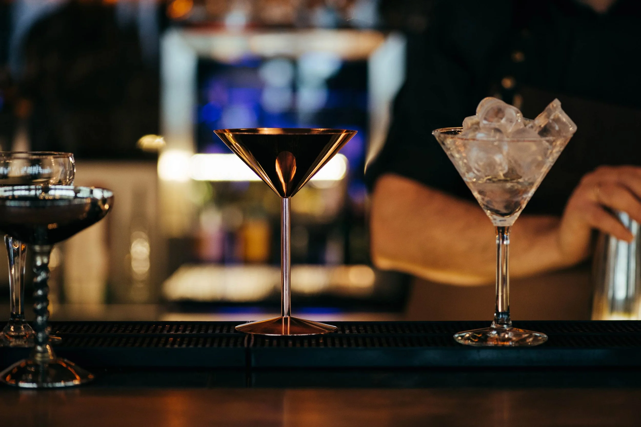 Vasos de cóctel y una hielera con hielo en un bar nocturno.