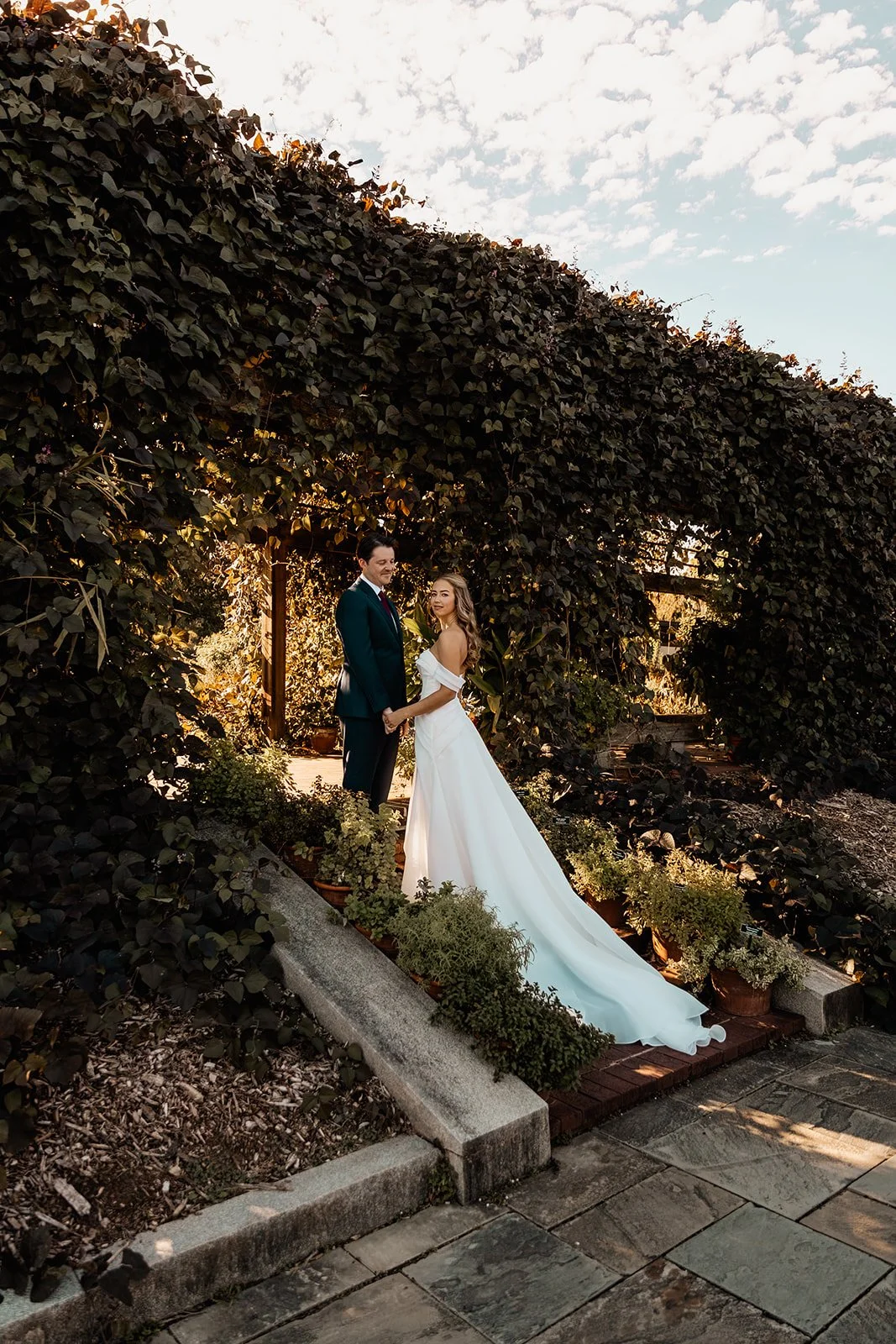 Bride and groom holding hands under a large leafy arch during their wedding photoshoot.