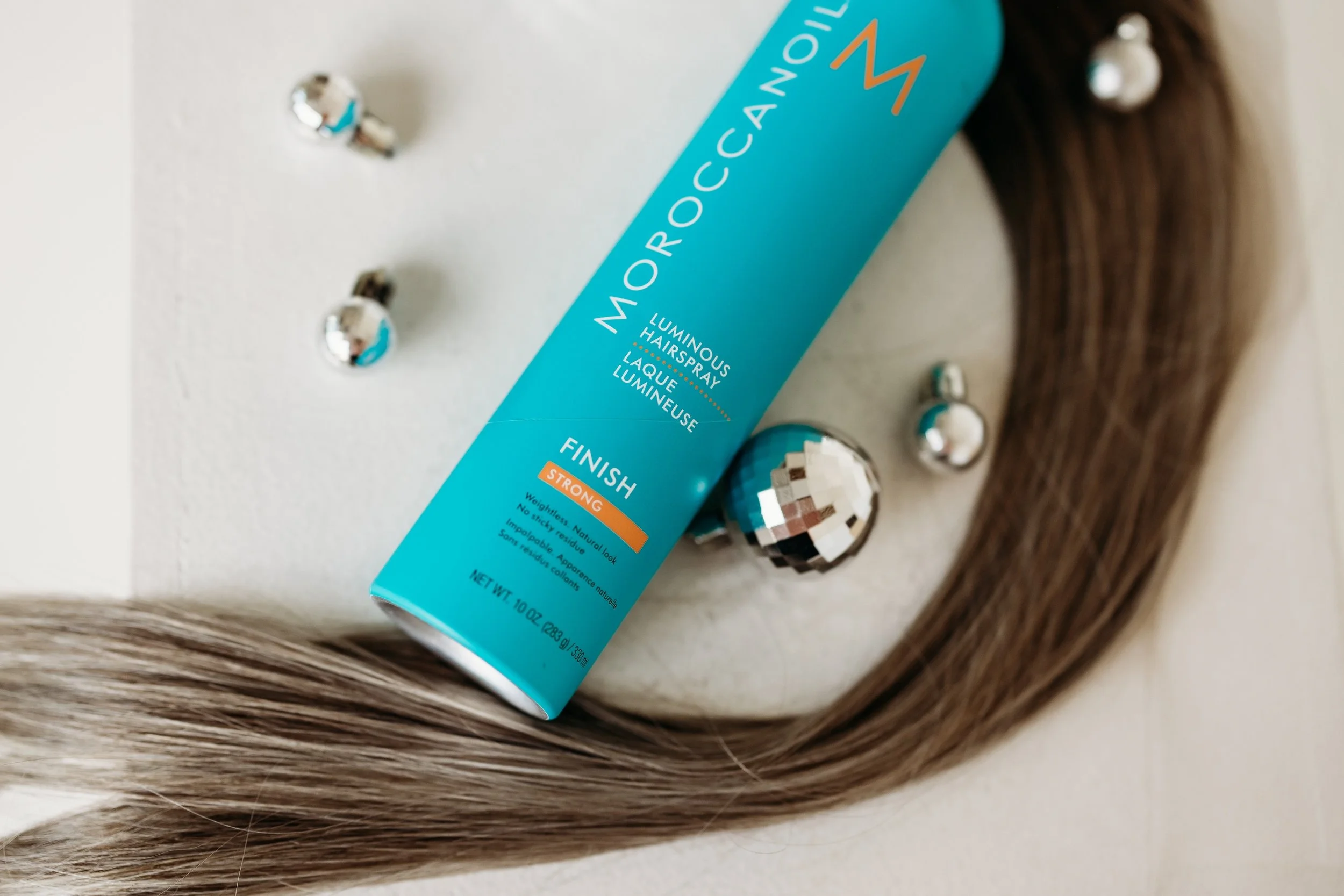 Moroccan oil hairspray next to a thick strand of brown hair.