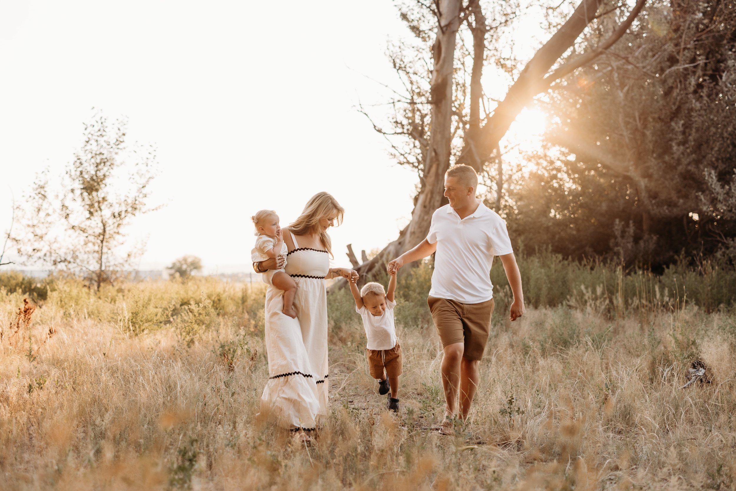 A family of four walking in a field at sunset.