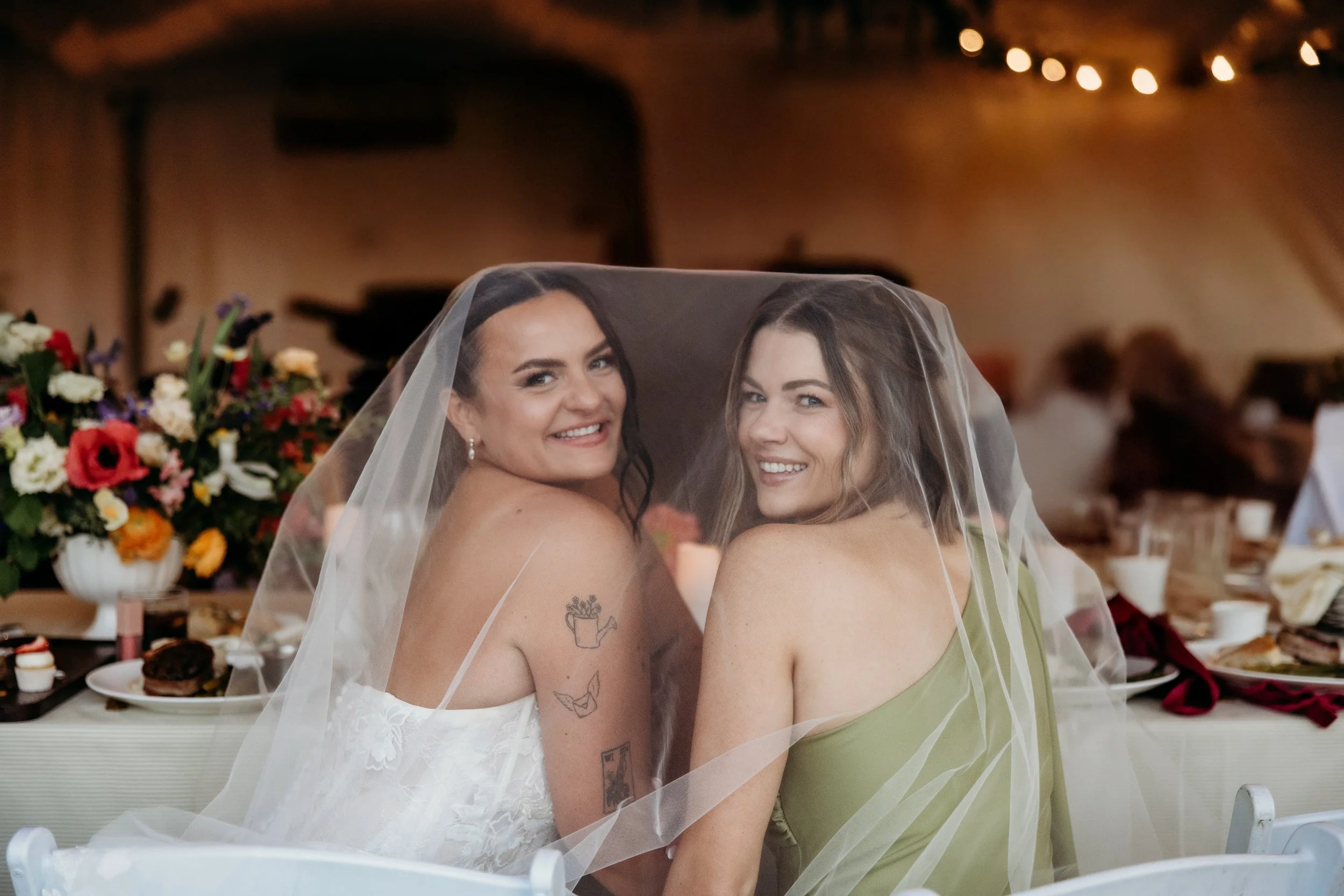 Bride and bridesmaid smiling under the veil.