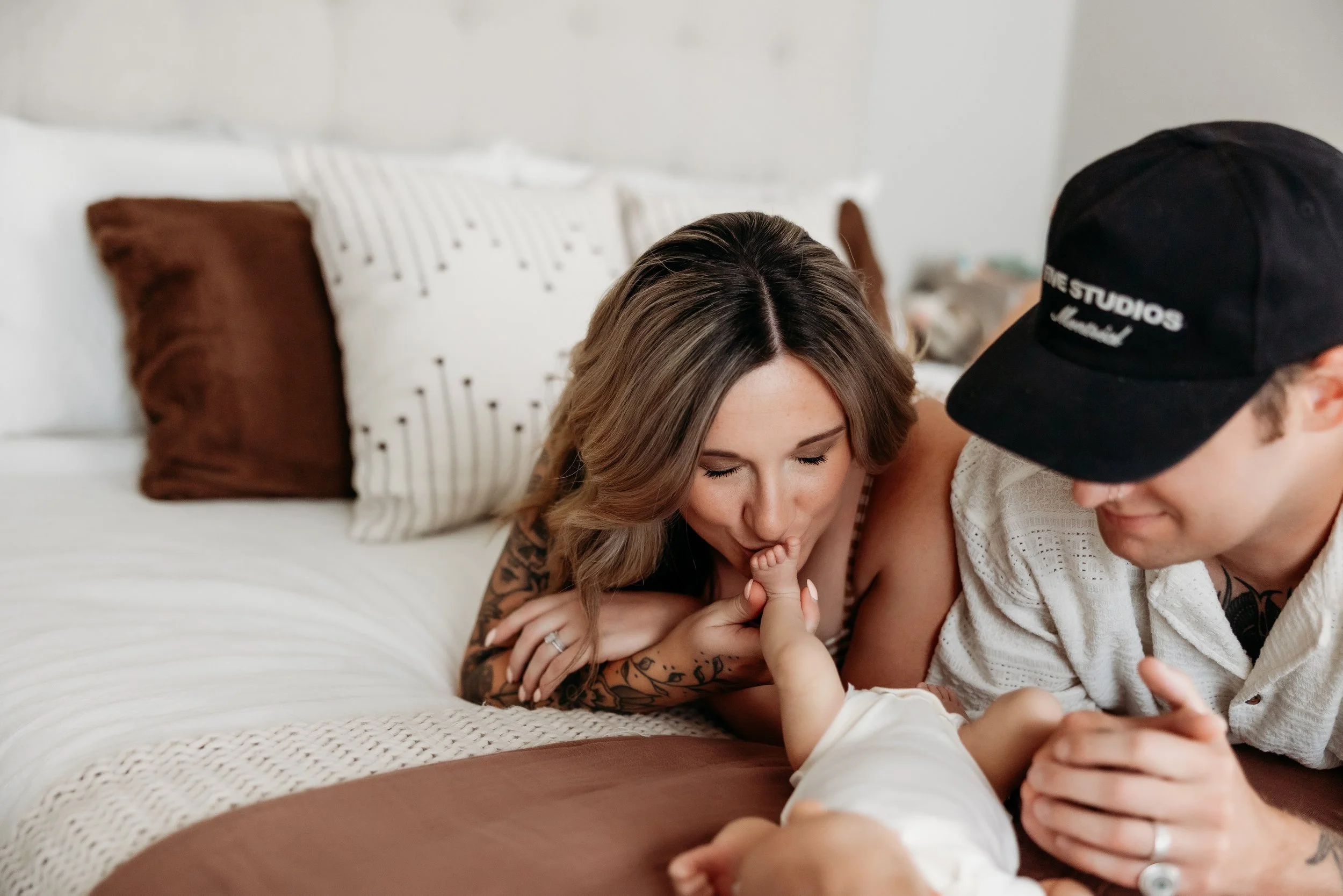Mother kissing her newborn baby's toes on a bed.