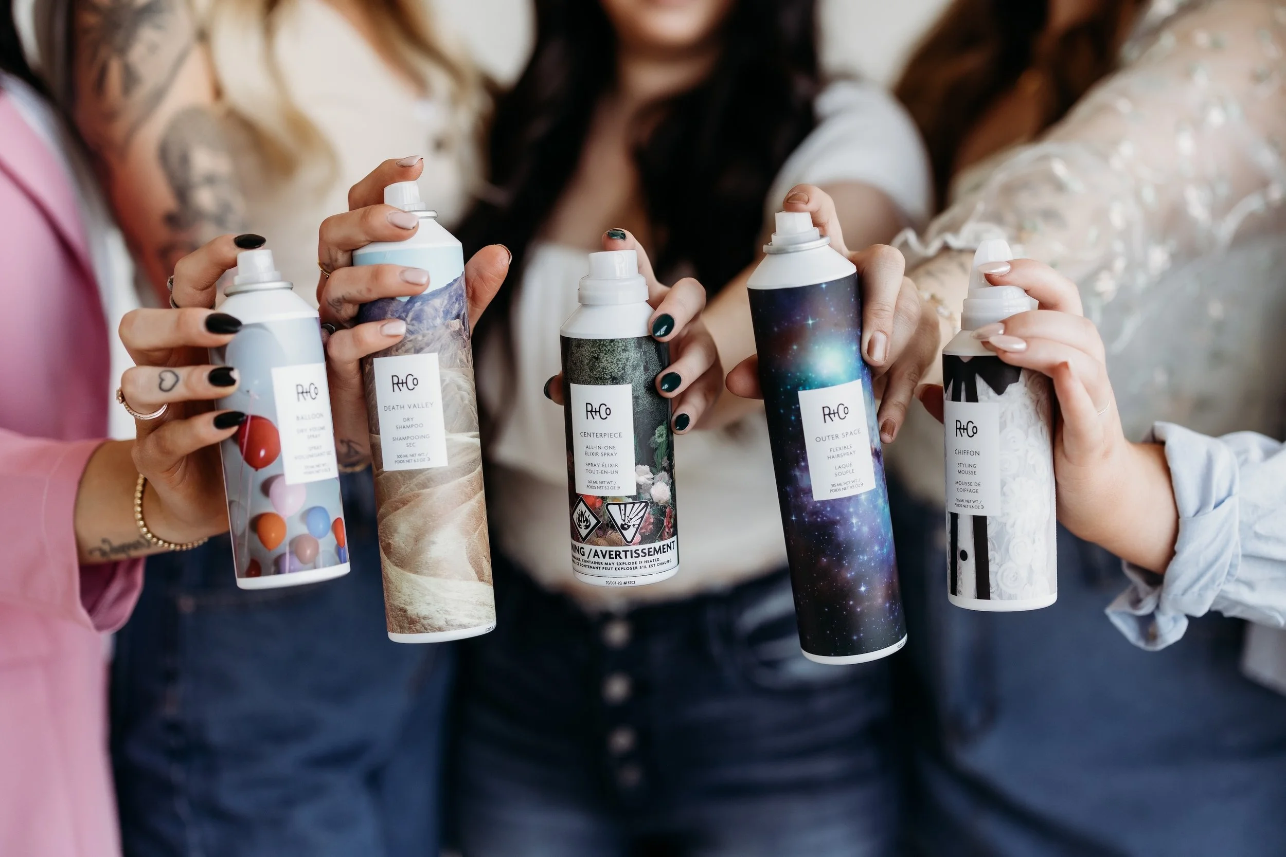 Five women holding different R and Co hair products.