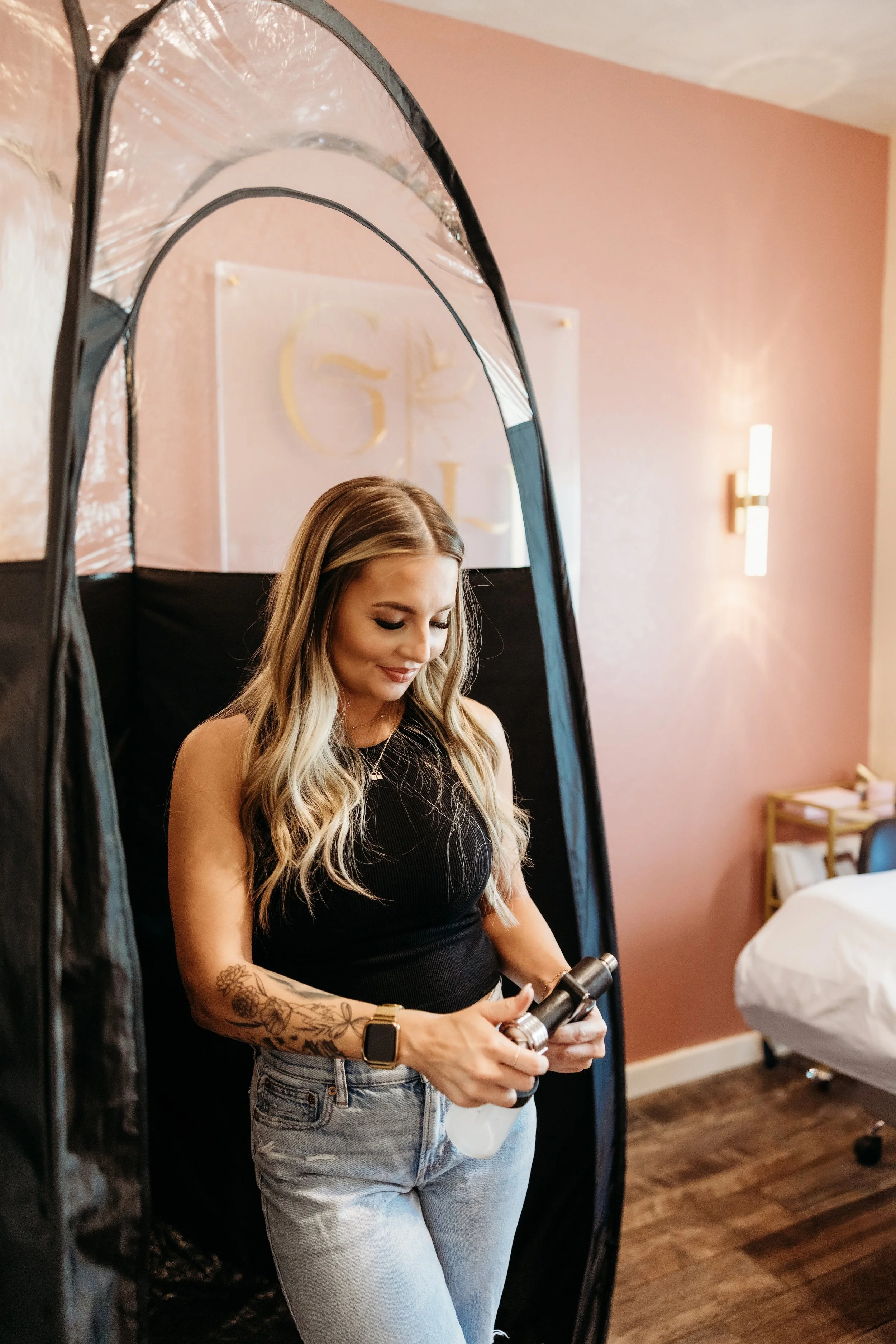 Woman holding a spray tan tool in front of a tent.