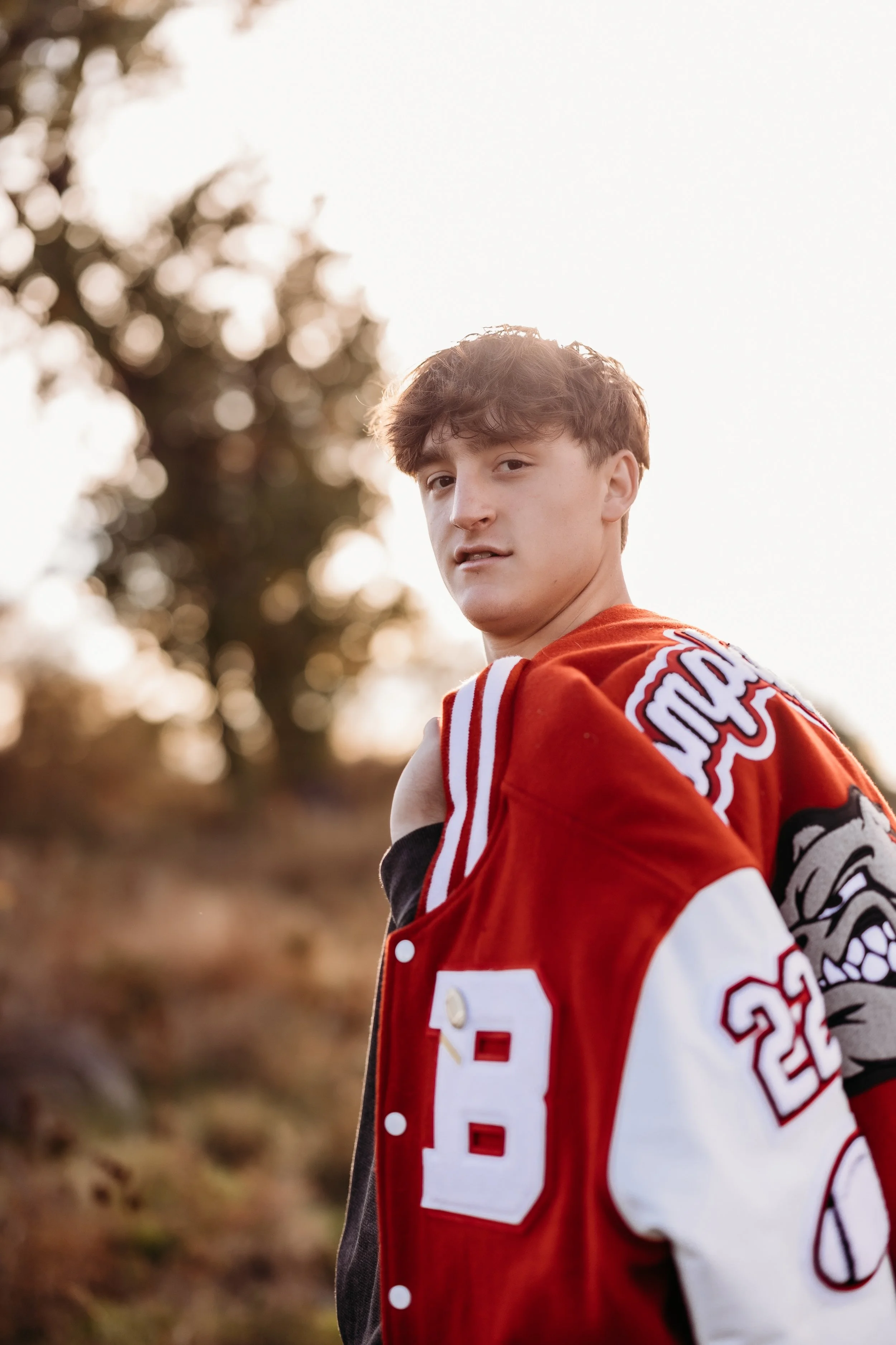 Teenage boy holding a letterman's jacket over his shoulder.