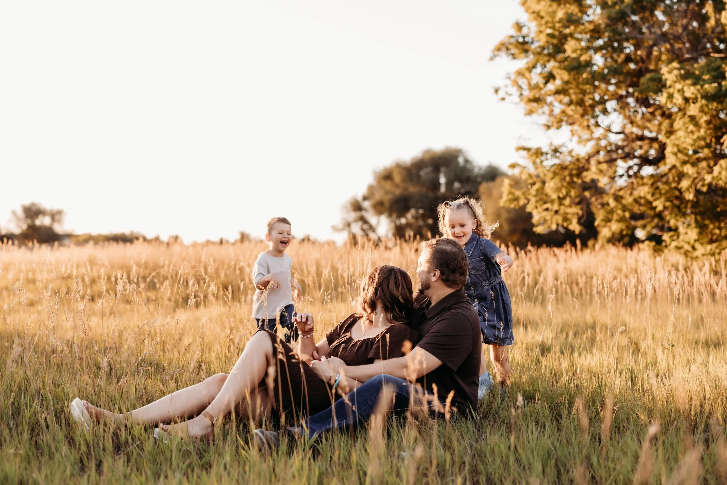 Two parents playing with their two kids in a field at sunset.
