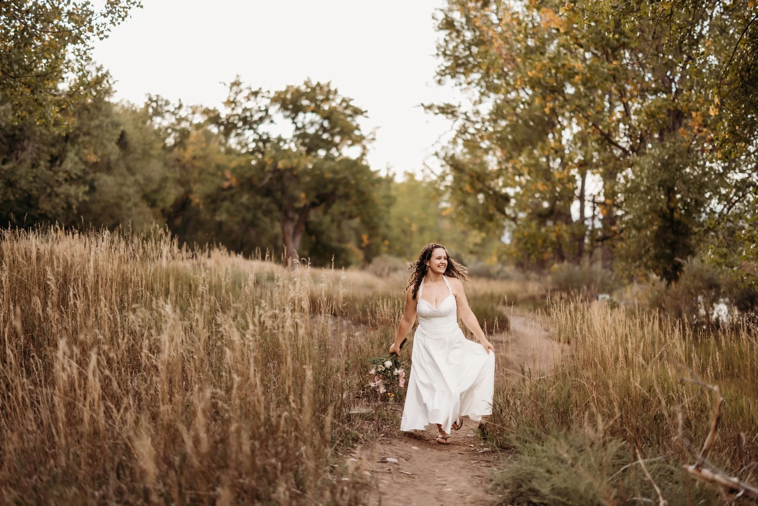 Girl in a flowing white dress walking through a field at East Lake Park in Thornton, Colorado.