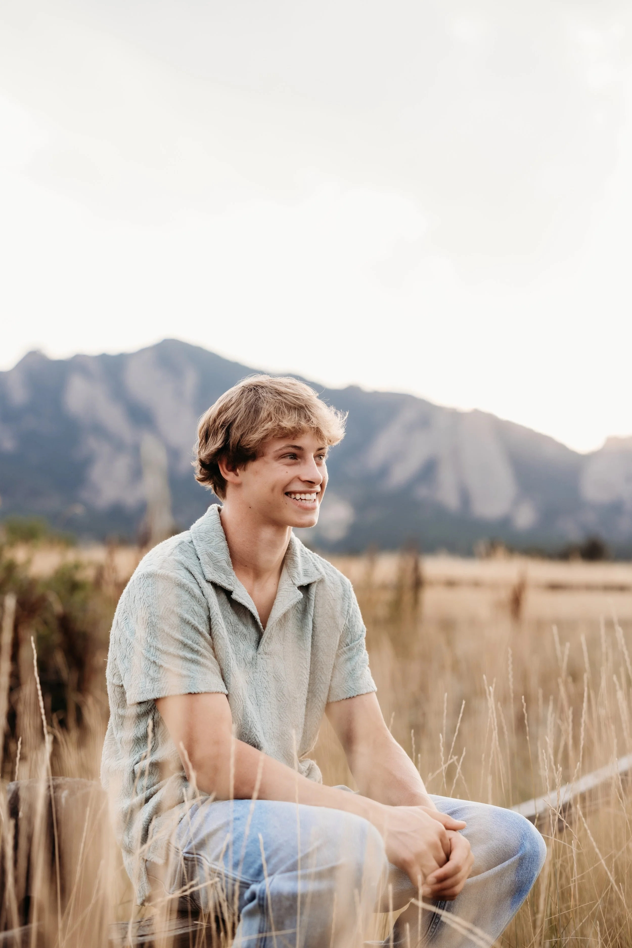 Teenage boy sitting and smiling in a field.