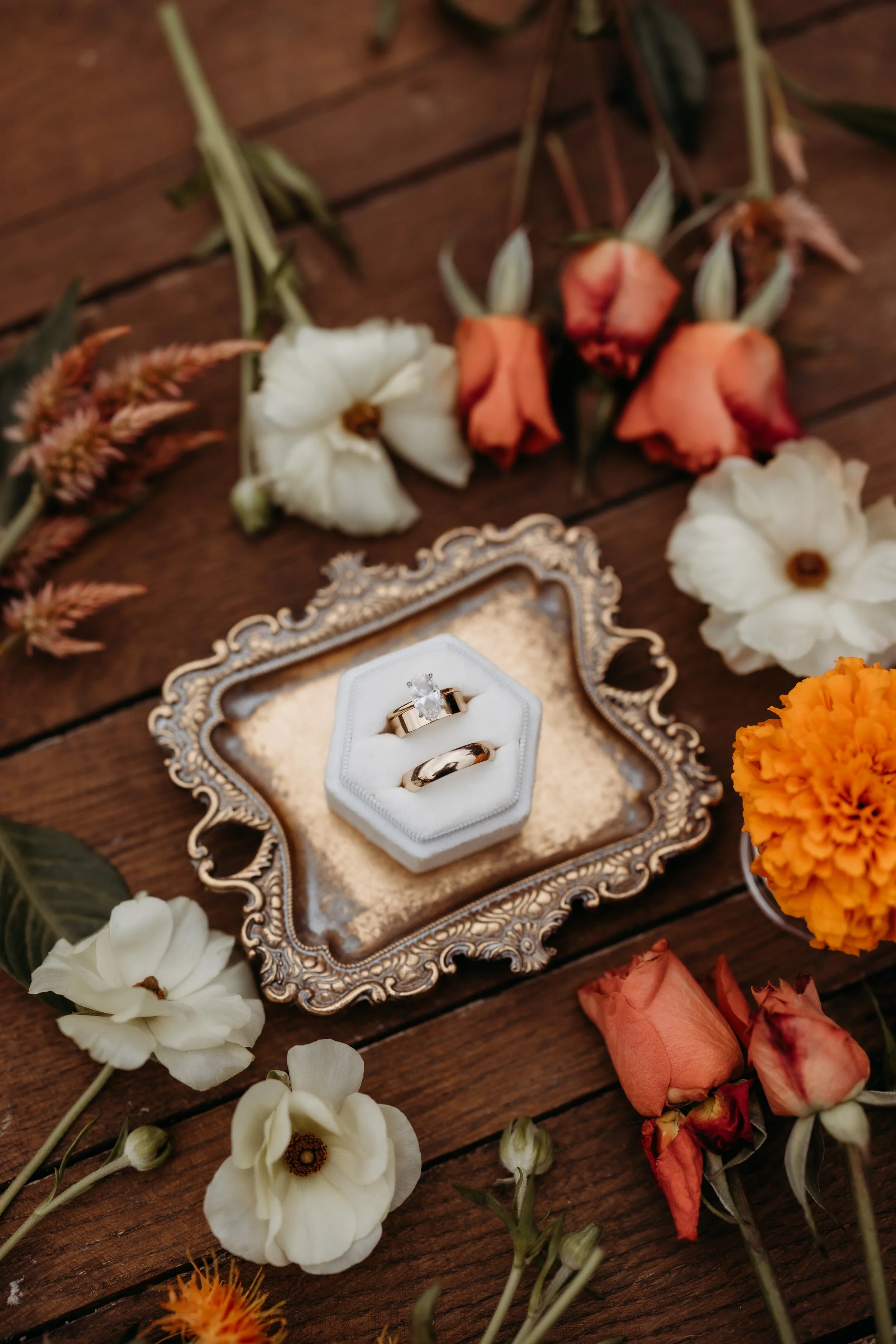 Bride and groom's wedding rings in a box surrounded by flowers.