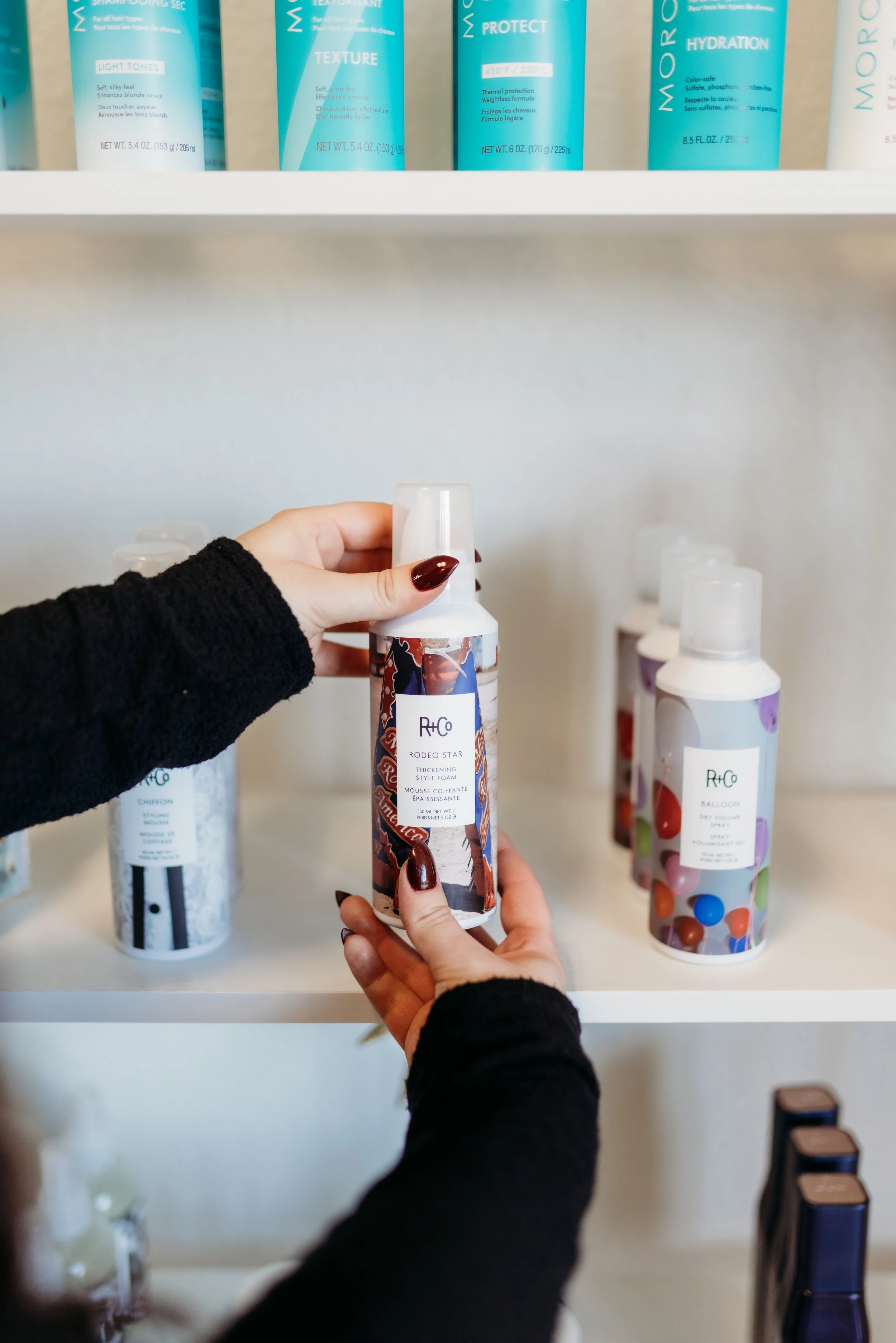 Holding a hair product in front of a shelf.