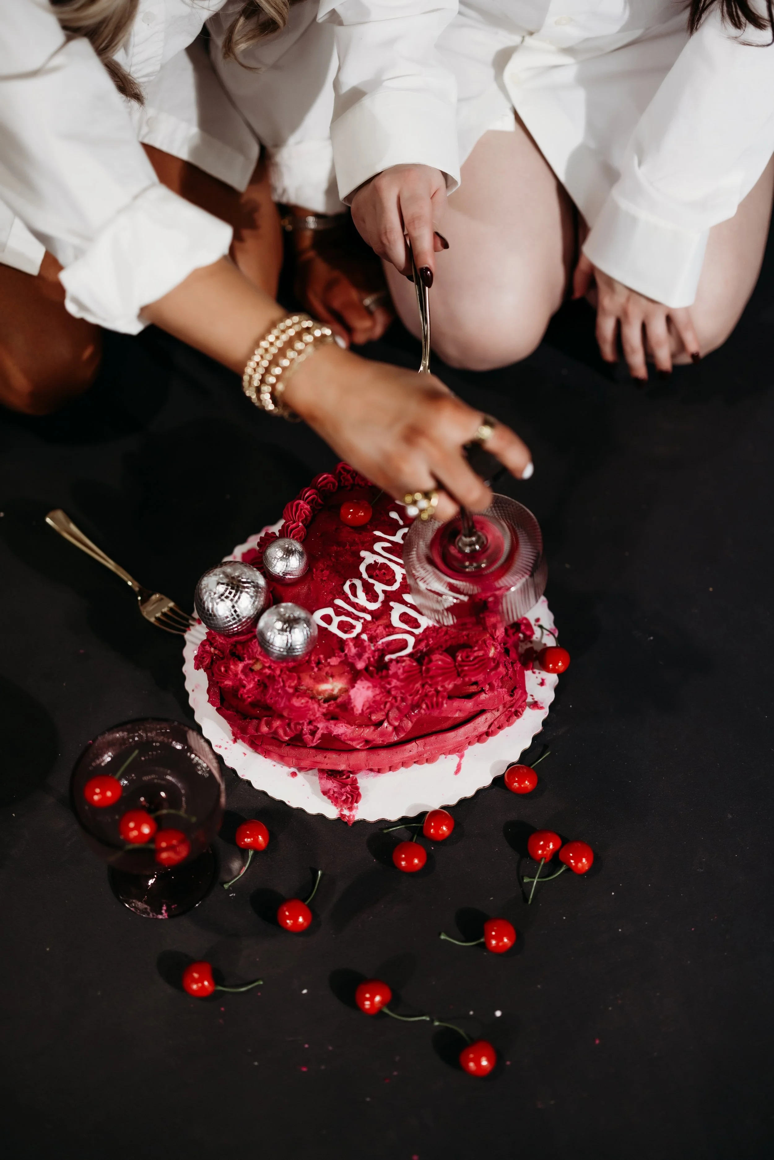 Cutting into a red cake on a black floor.