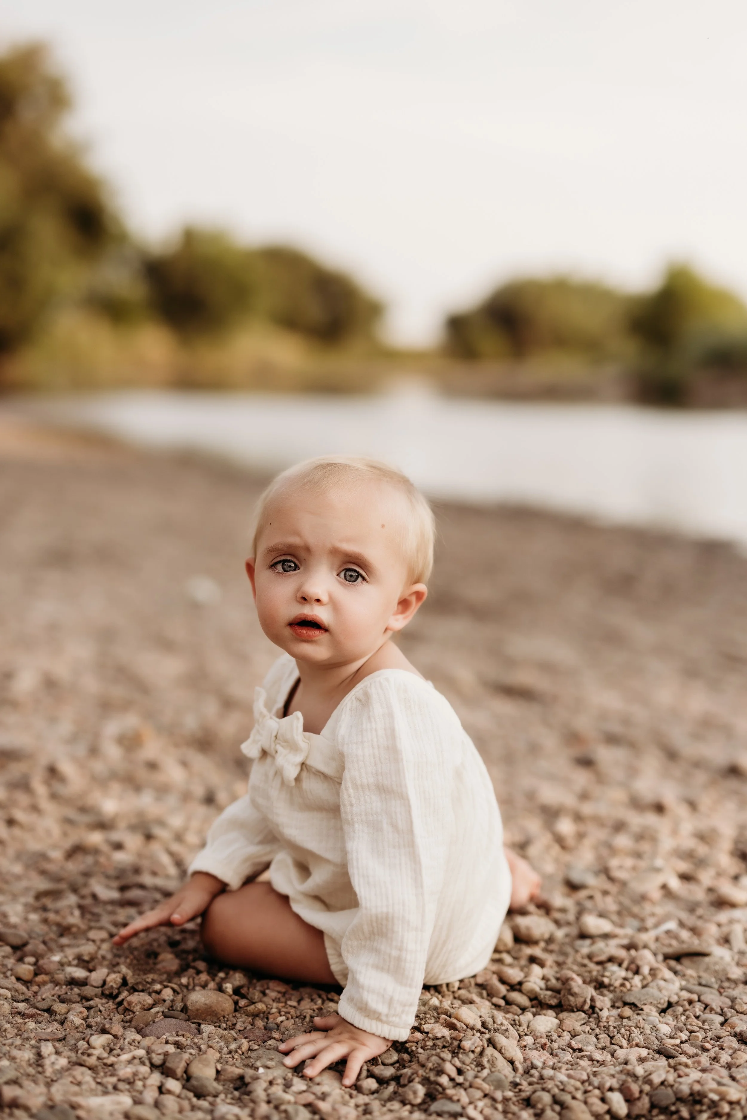 Toddler sitting on a rocky shore at a lake in Brighton, Colorado.